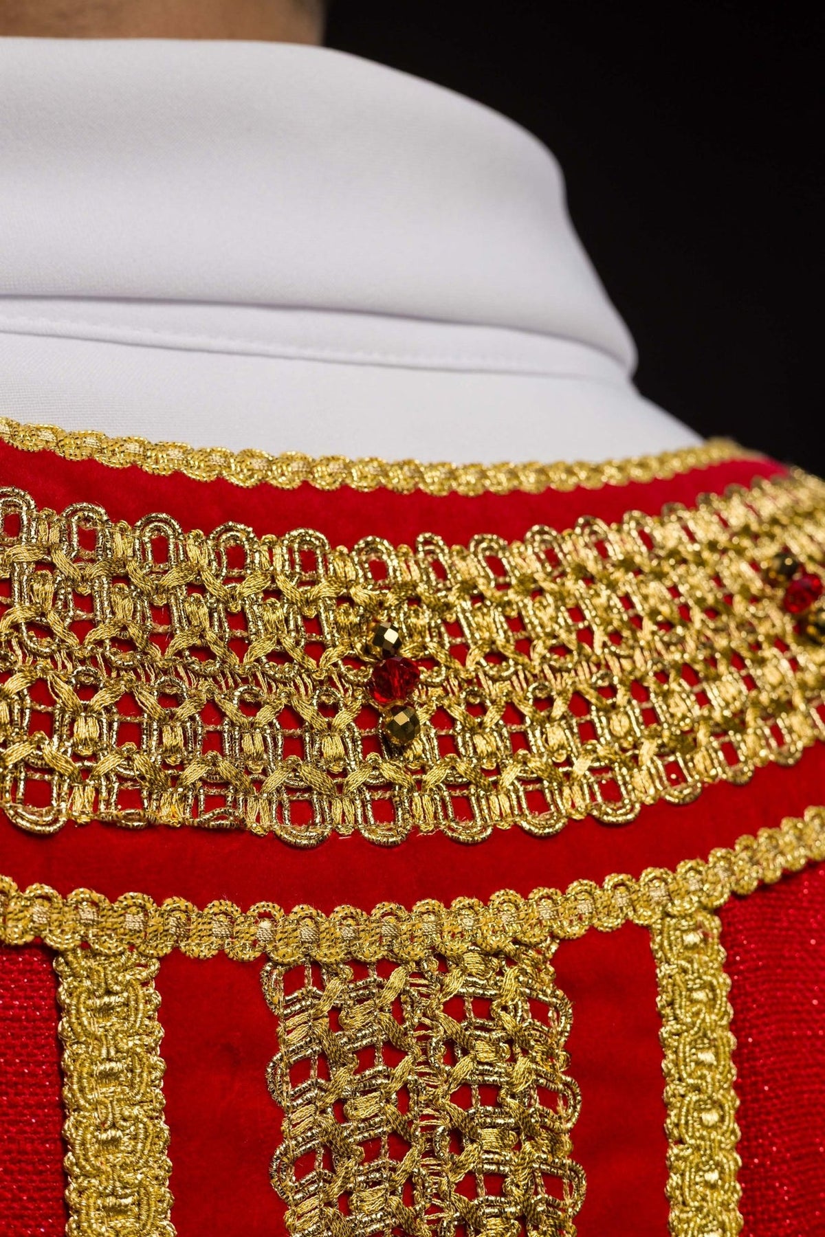 Handcrafted chasuble close-up of gold collar embroidery and natural stones on red fabric