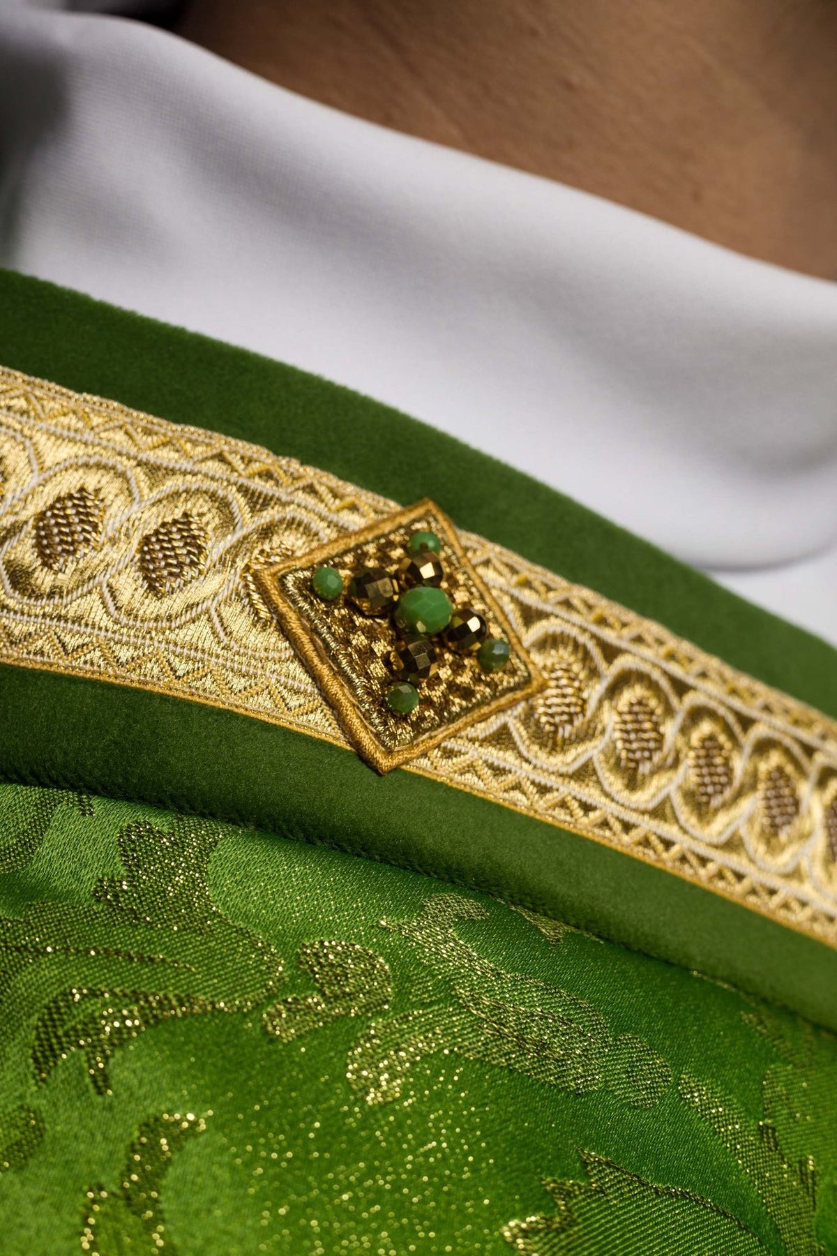 Green chasuble close-up showing gold edging, jacquard pattern and stone details