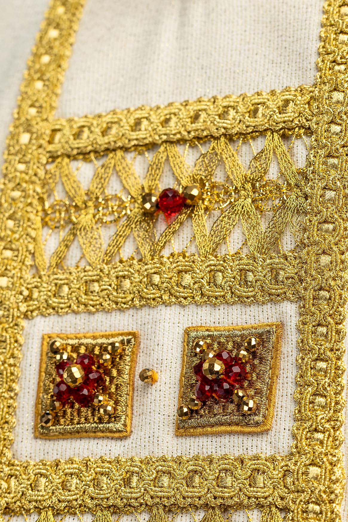 Handcrafted chasuble close-up of gold openwork trim and a red stone