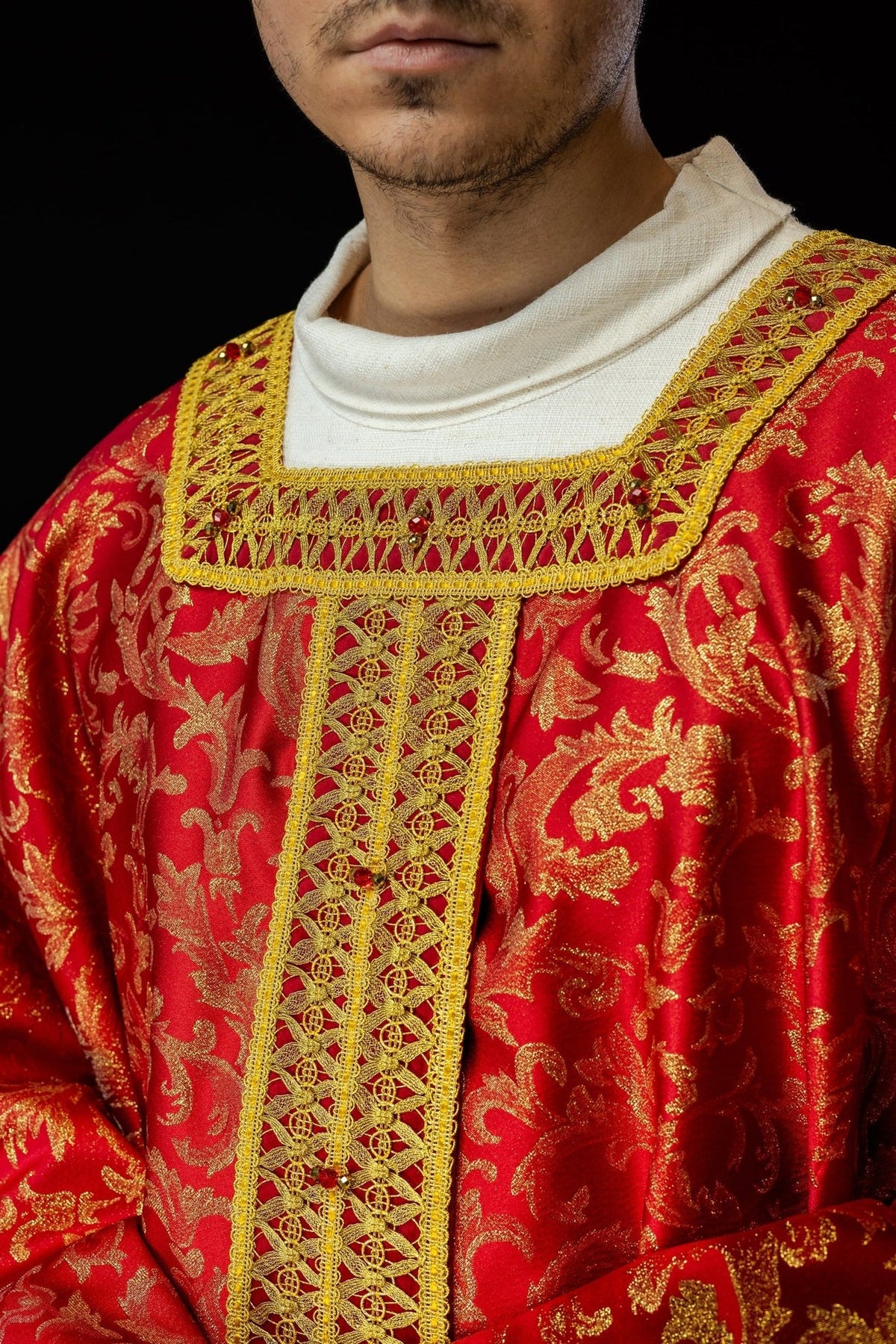 Red chasuble close-up showing gold embroidery, natural stones and central orphrey
