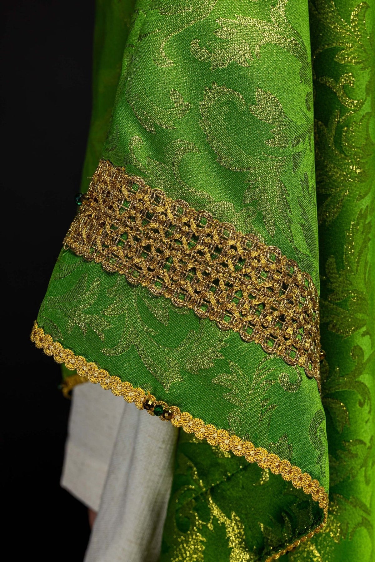 Green chasuble side close-up showing gold trim, jacquard fabric and stones