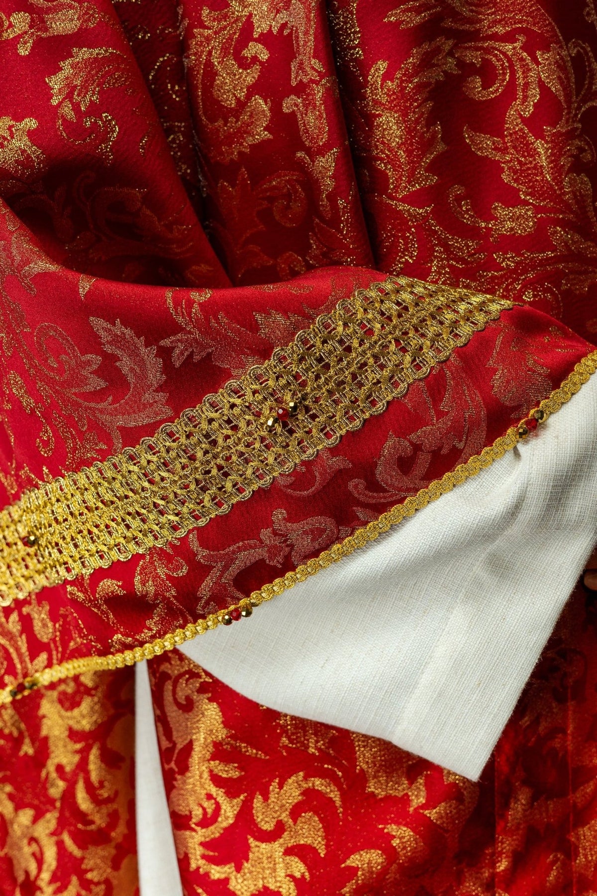 Red chasuble close-up of gold floral jacquard fabric and sleeve trim