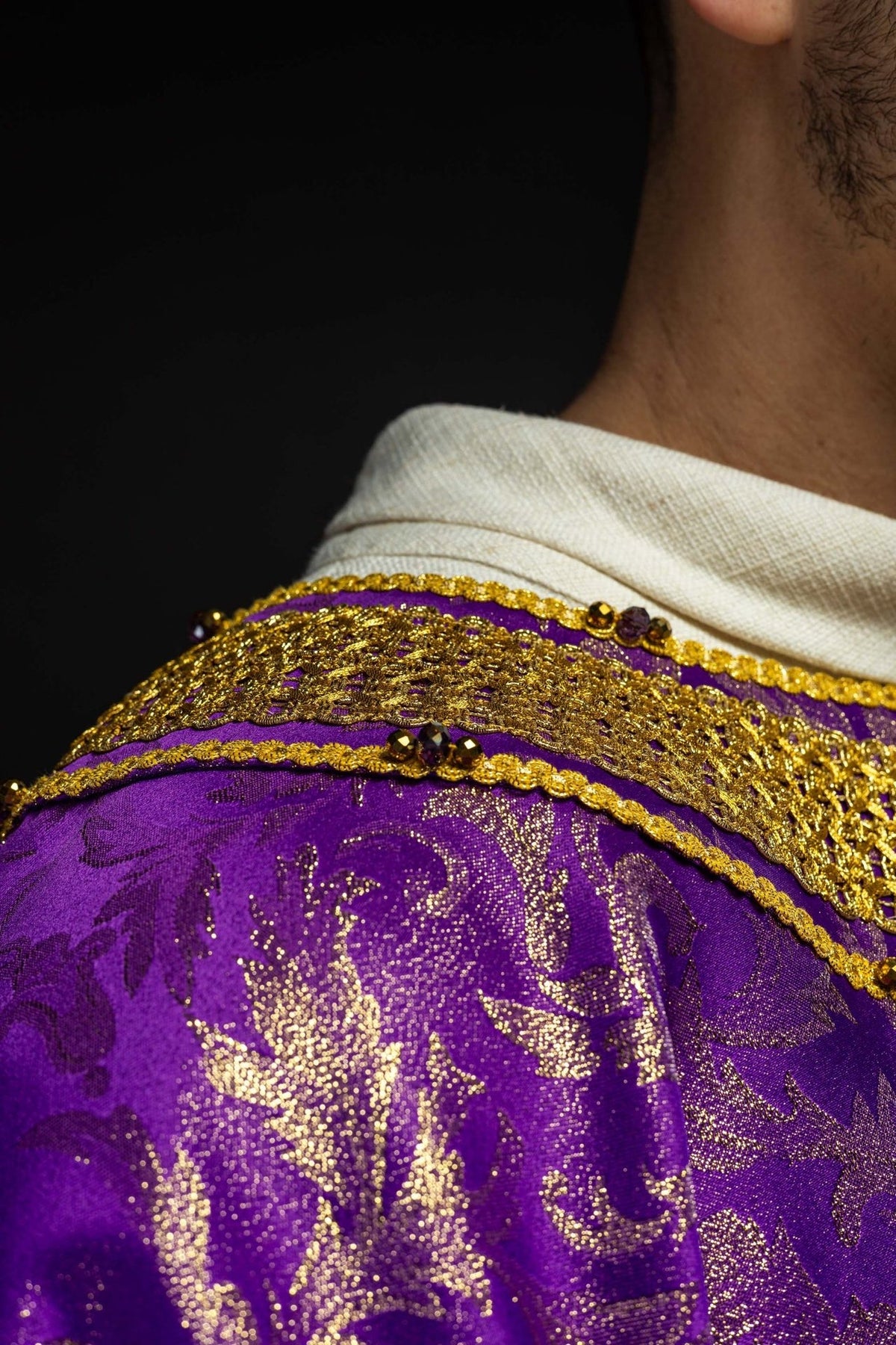 Purple chasuble shoulder close-up with gold embroidery, trim and natural stones