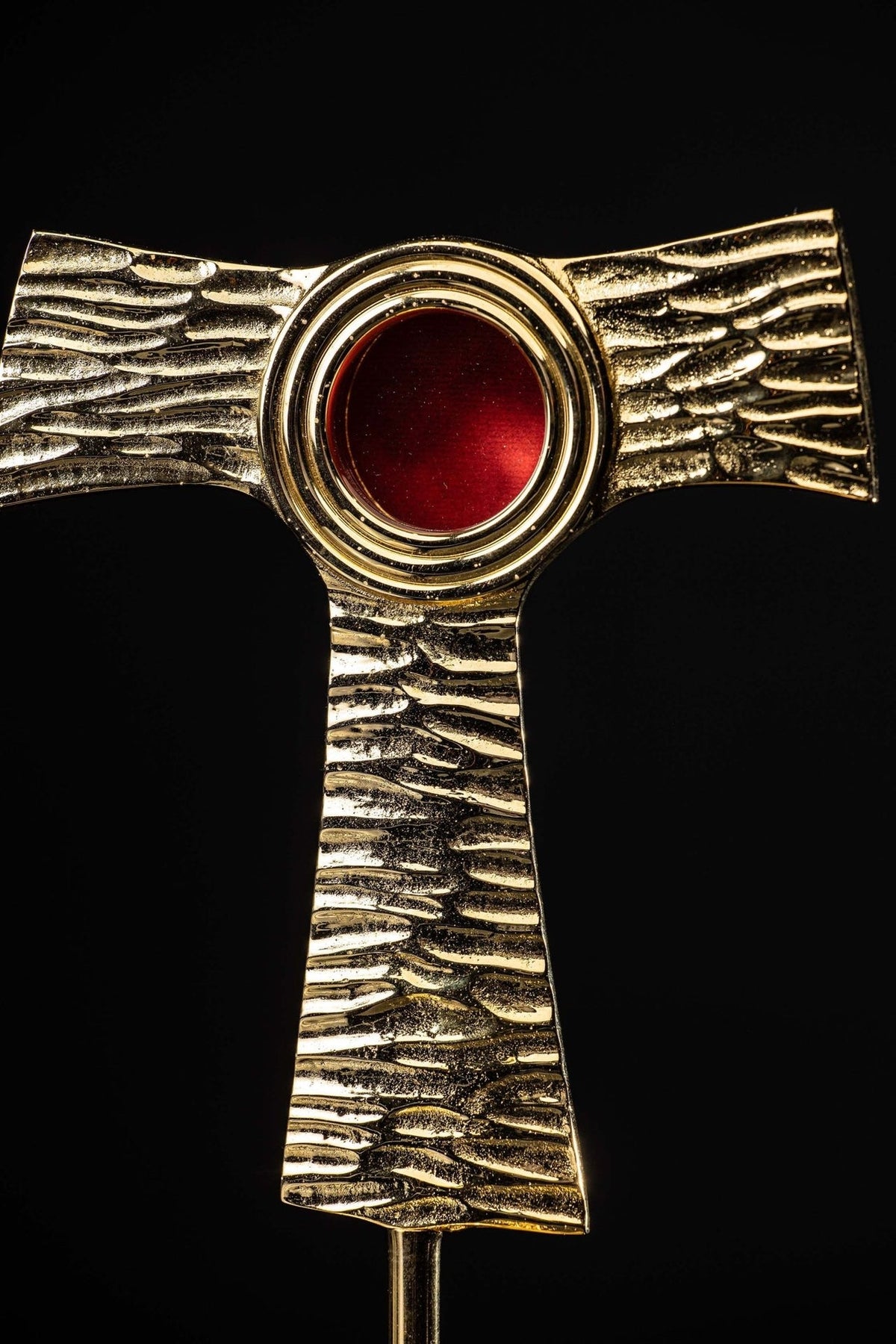 Tau cross reliquary close-up showing textured gold brass arms and red repository