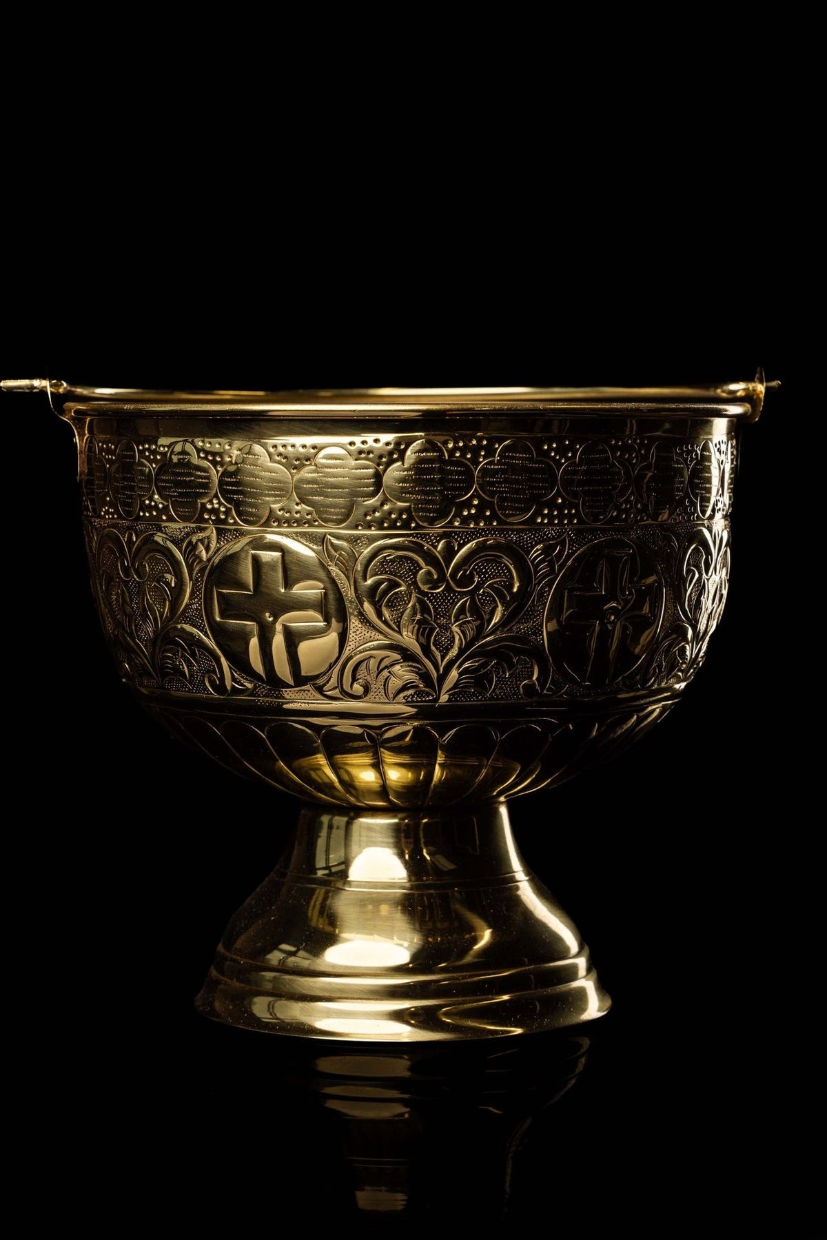Brass holy water bucket close-up showing engraved crosses, floral motifs and patterned upper band
