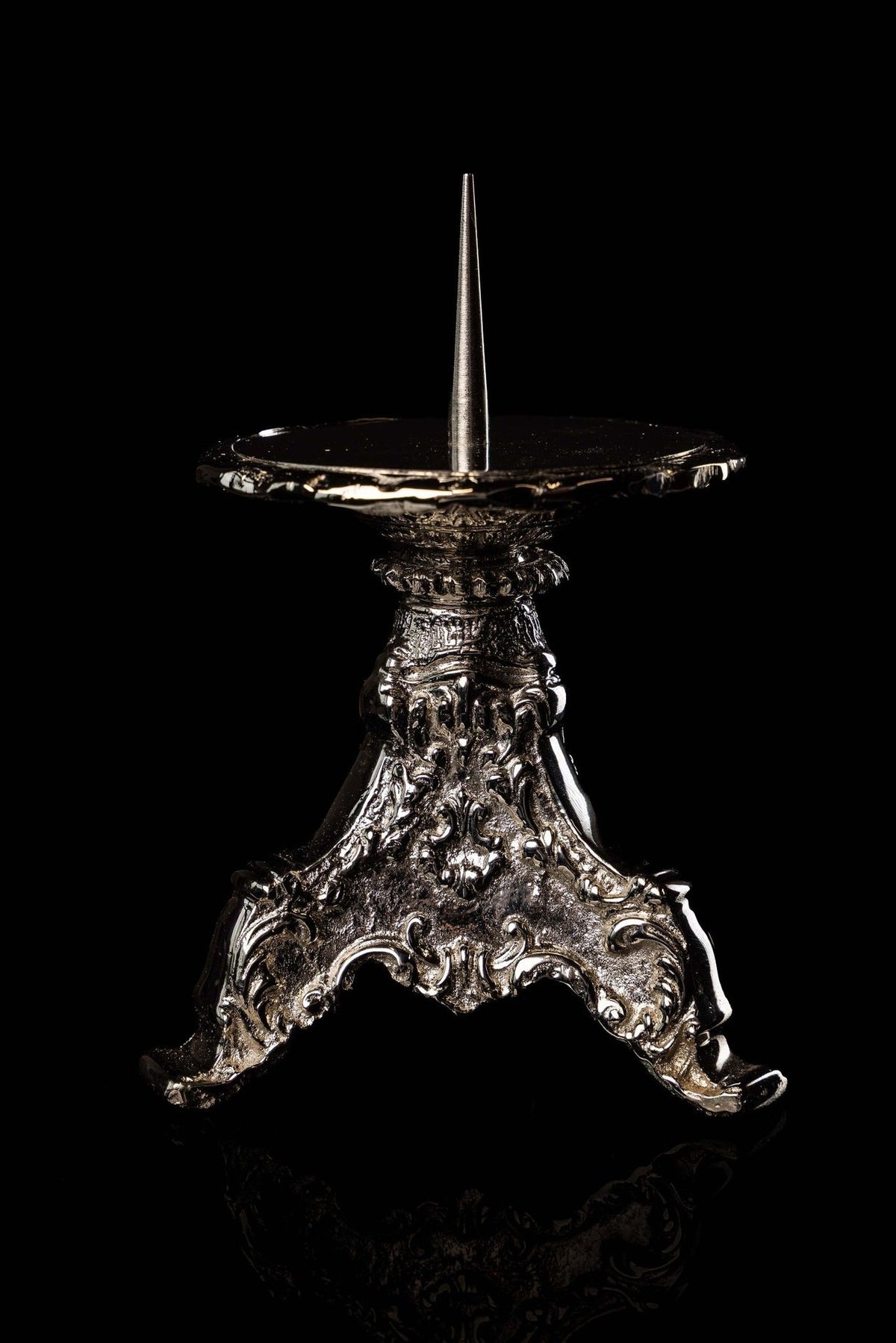 Nickel-plated brass candlestick close-up showing ornate relief and pointed candle spike