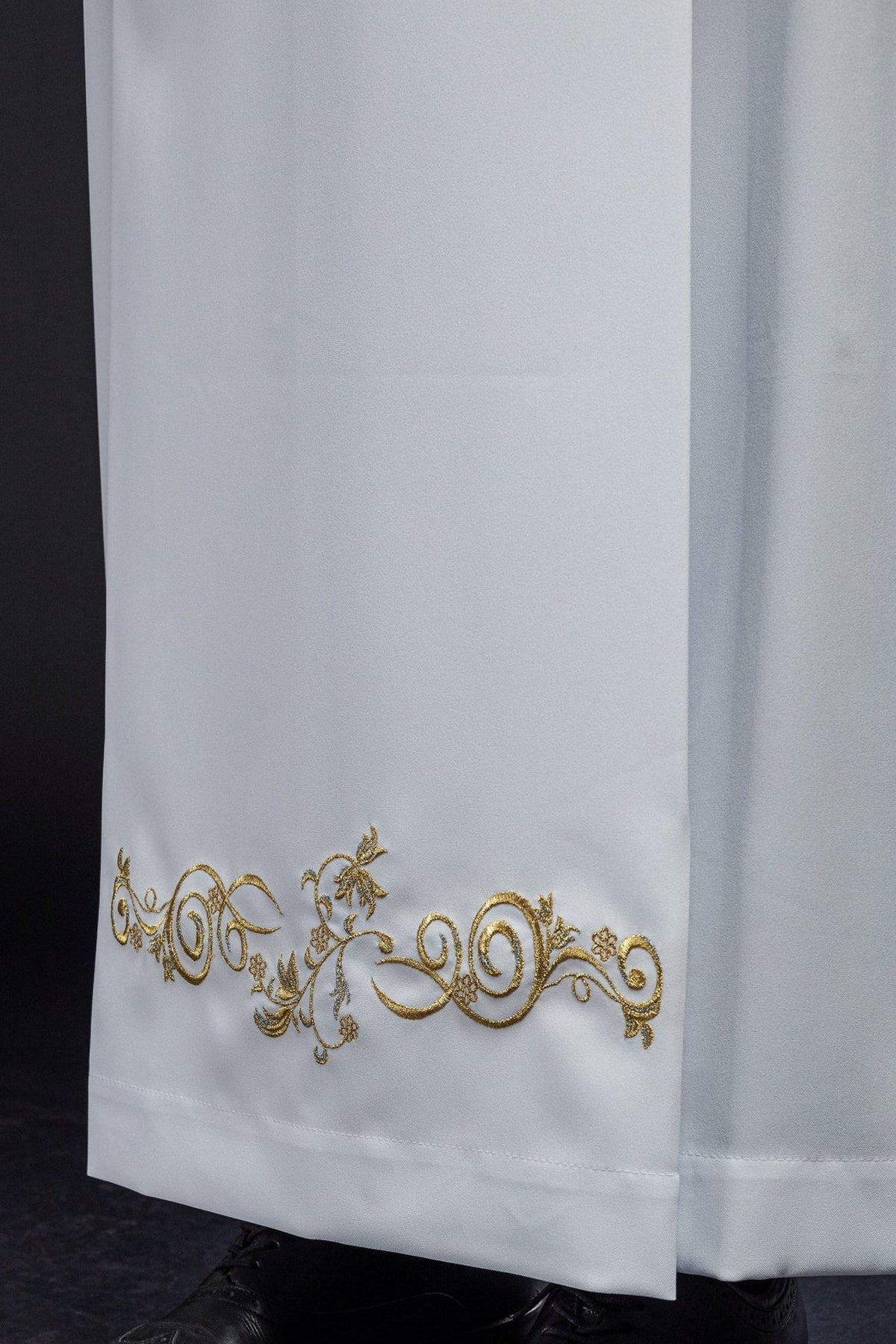 White priest alb close-up showing gold embroidered hem detail