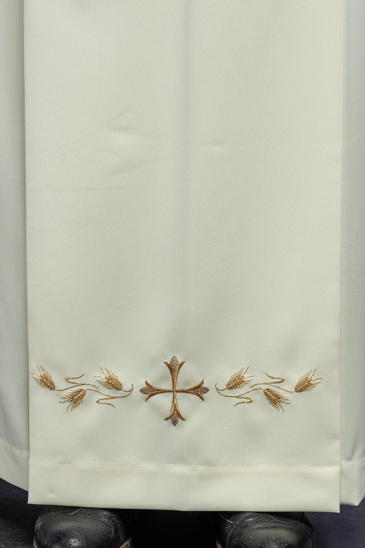 Ecru priest alb close-up of gold cross and wheat embroidery at the hem