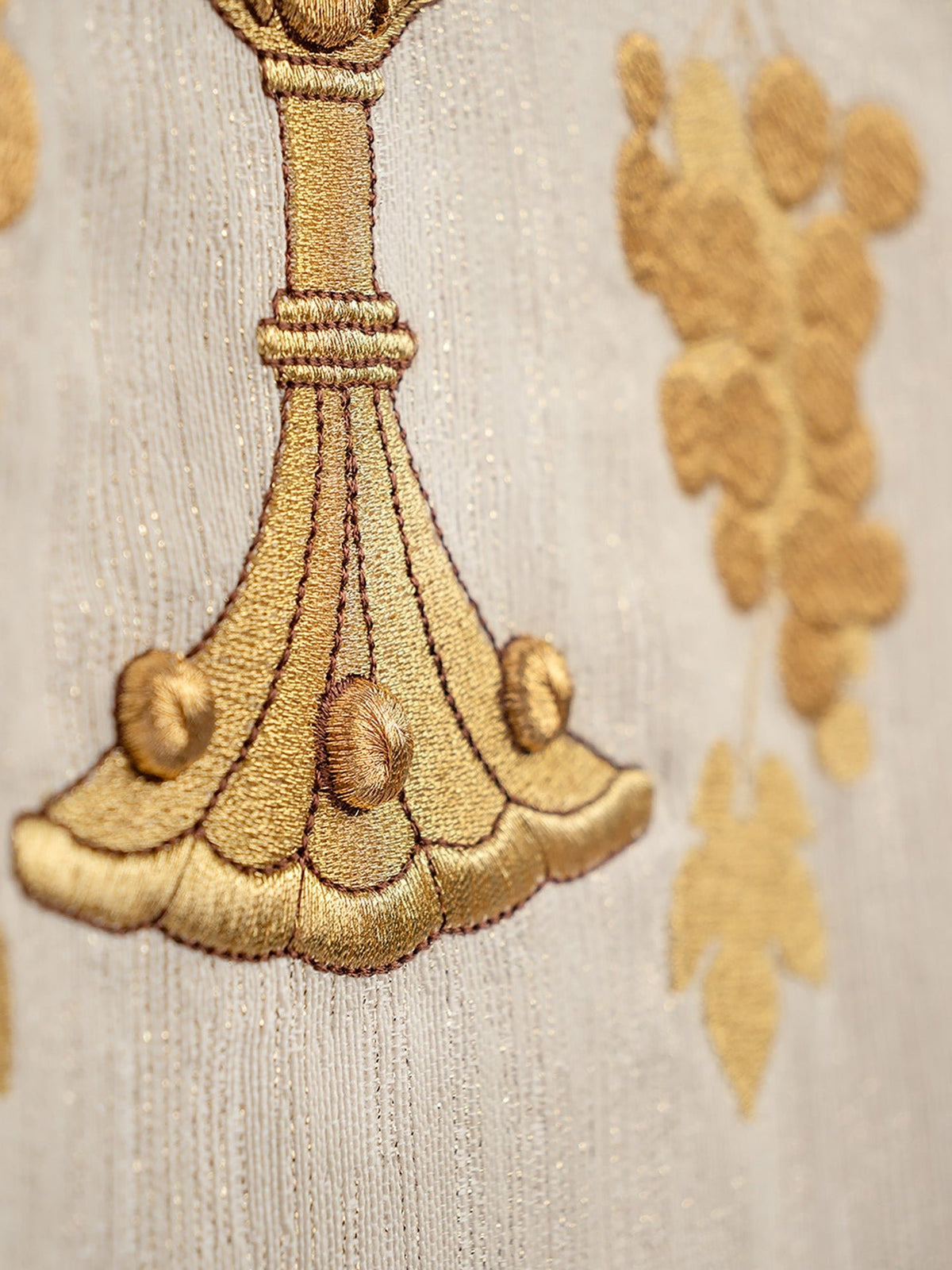 Gold embroidery close-up showing chasuble chalice base and grapes
