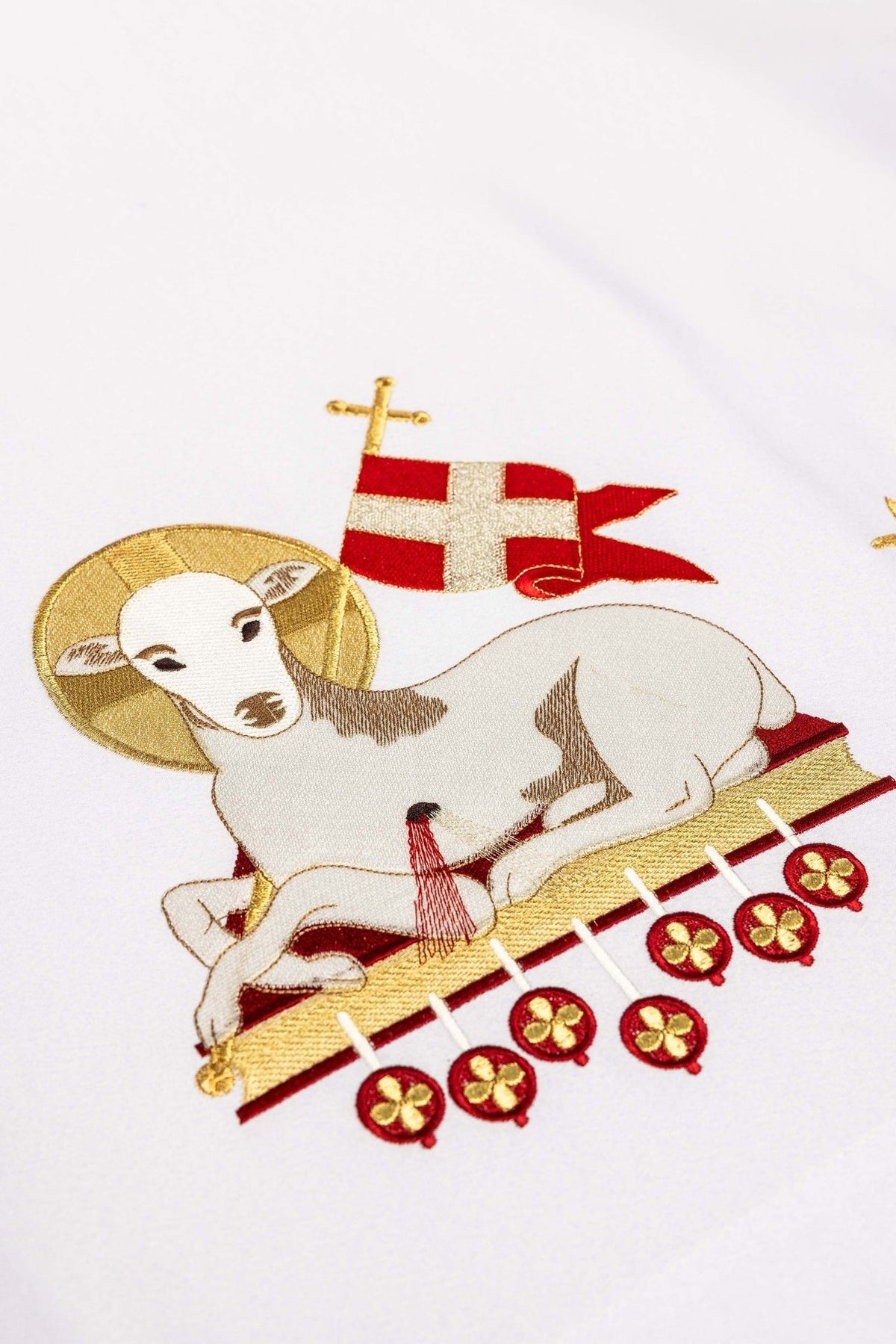 Altar cloth close-up of the Agnus Dei embroidery, showing its red banner, gold halo and hanging motifs