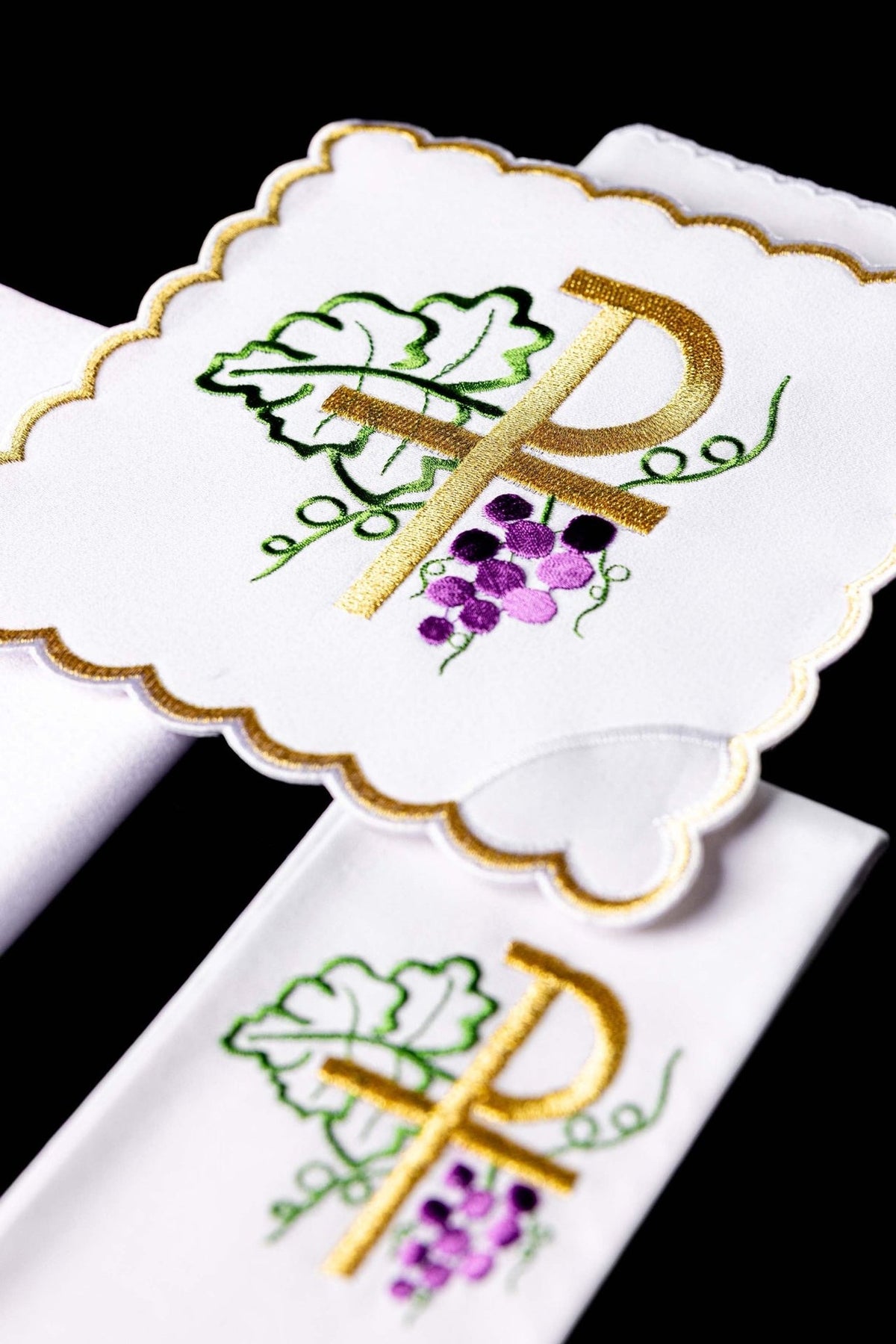Altar linen set close-up showing embroidered gold PAX, green leaves, and purple grapes
