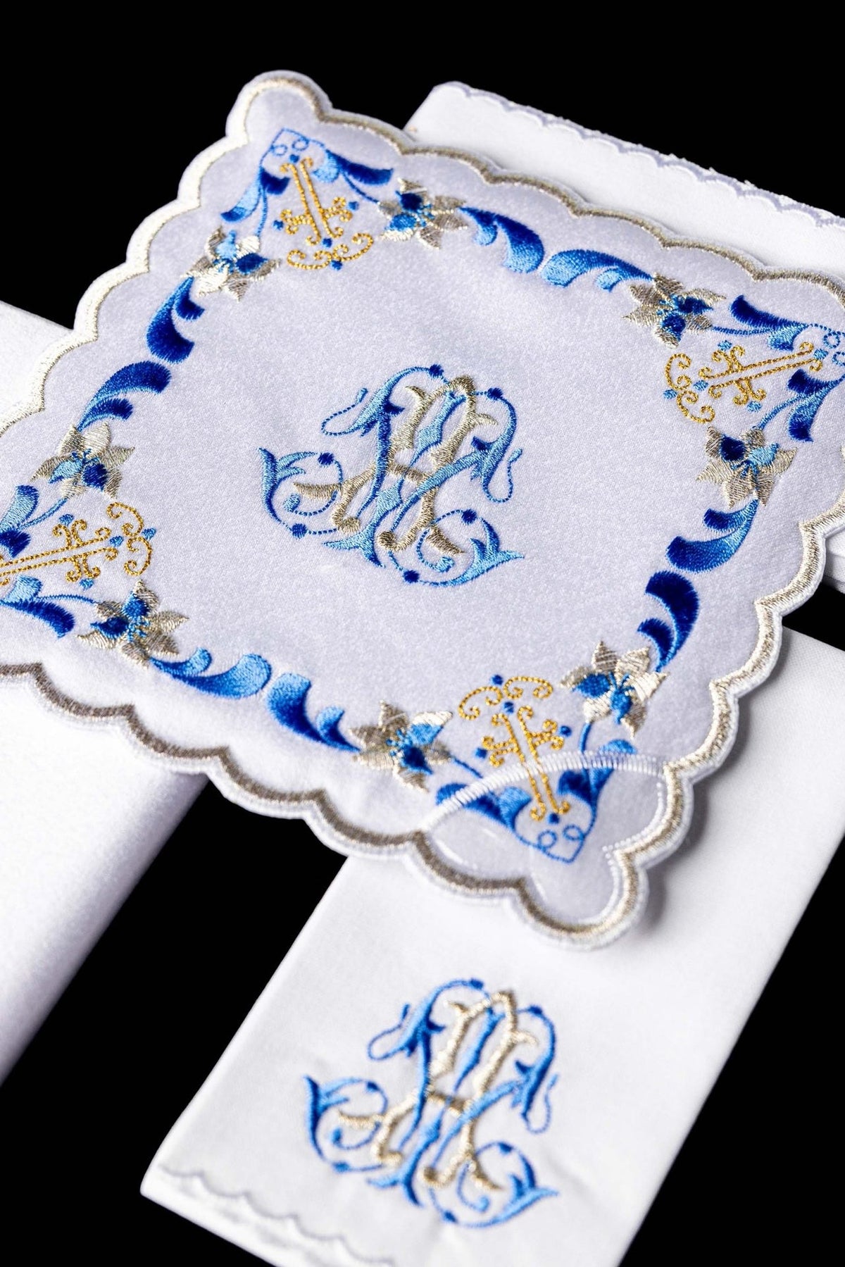 Altar linen set close-up showing blue and gold embroidered Marian symbol on a white cloth