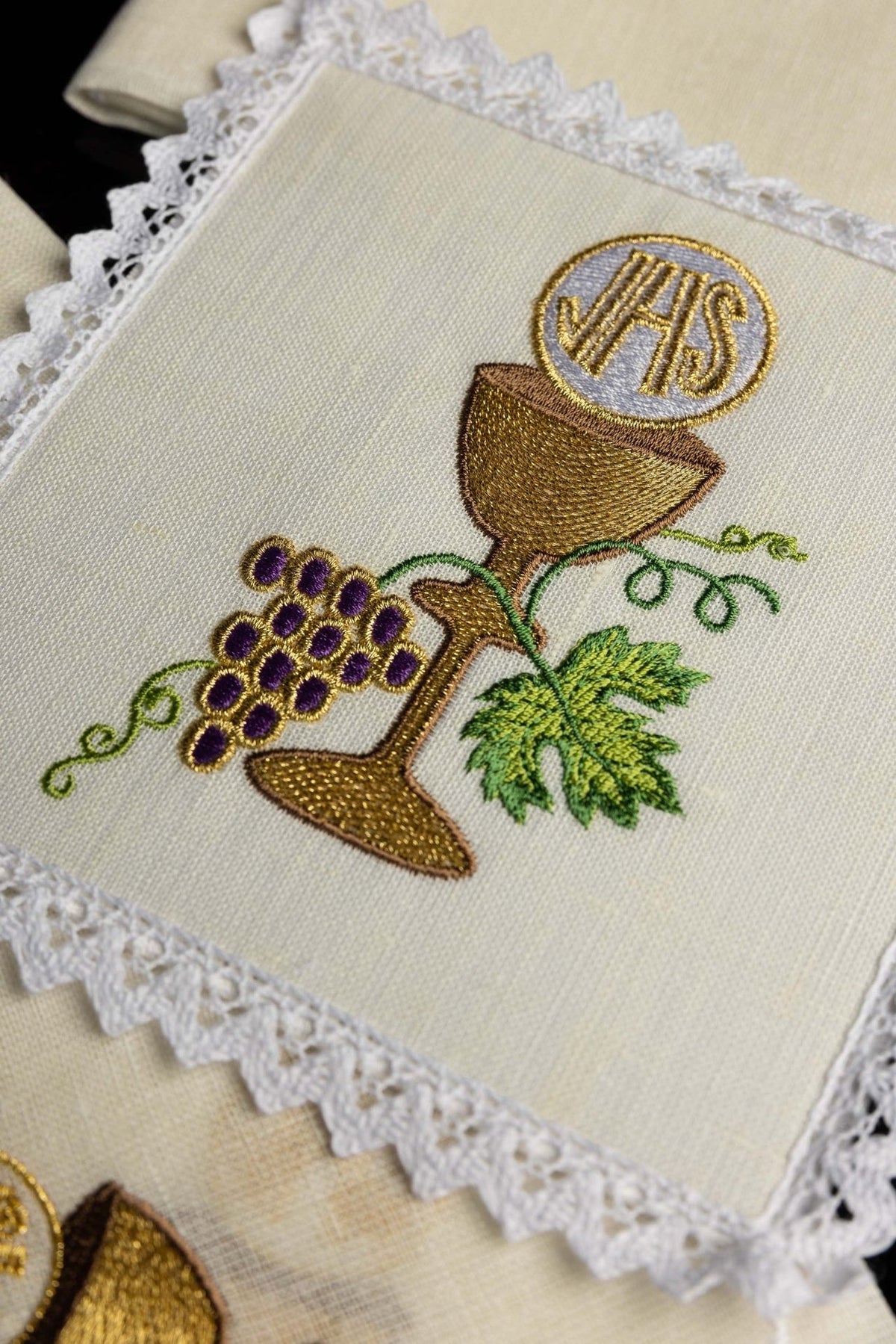 Altar linen set close-up showing embroidered gold chalice, grapes and green vine with white lace trim