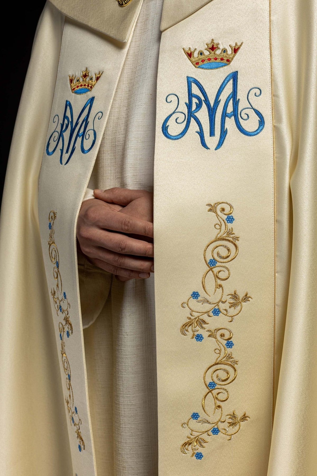 Marian cope embroidery close-up showing blue monogram, crowned emblem and gold floral details