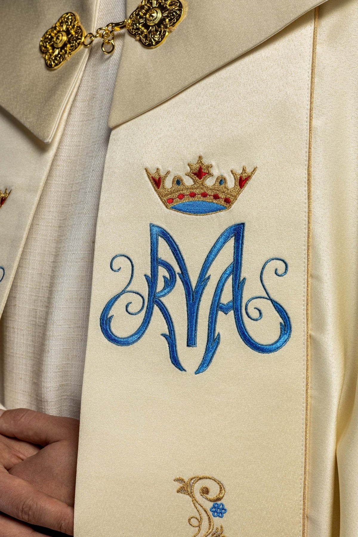 Marian cope embroidery detail with blue monogram and multicolour crowned emblem
