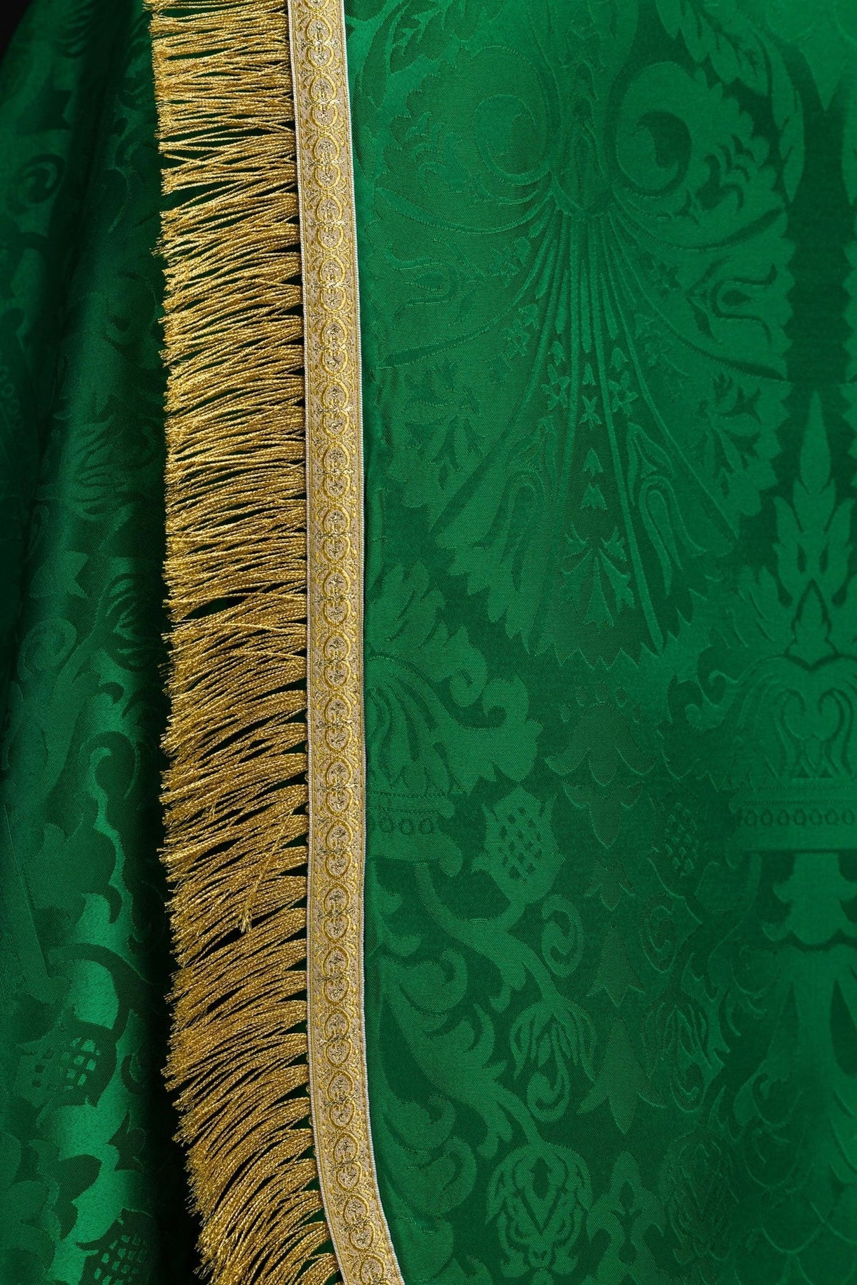 Green jacquard cope close-up showing gold trim, woven motifs and long gold fringe