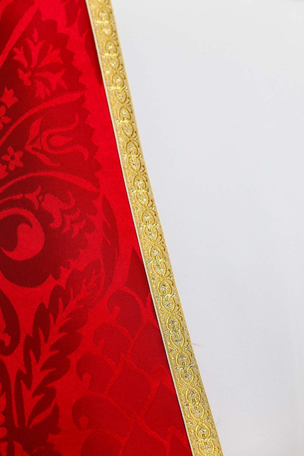 Red cope close-up showing smooth jacquard fabric, floral motifs and decorative gold edging