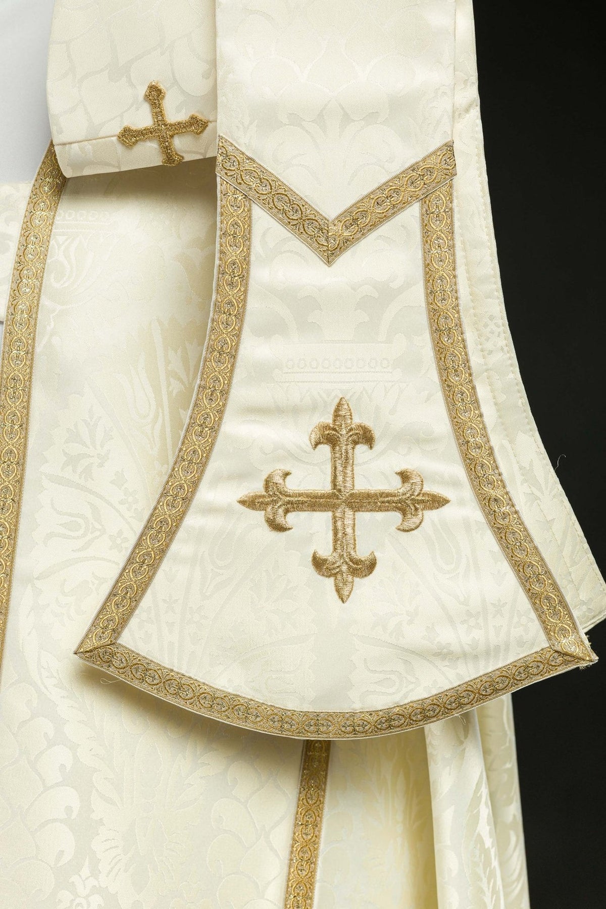 Ecru cope detail showing embroidered gold cross and decorative trim
