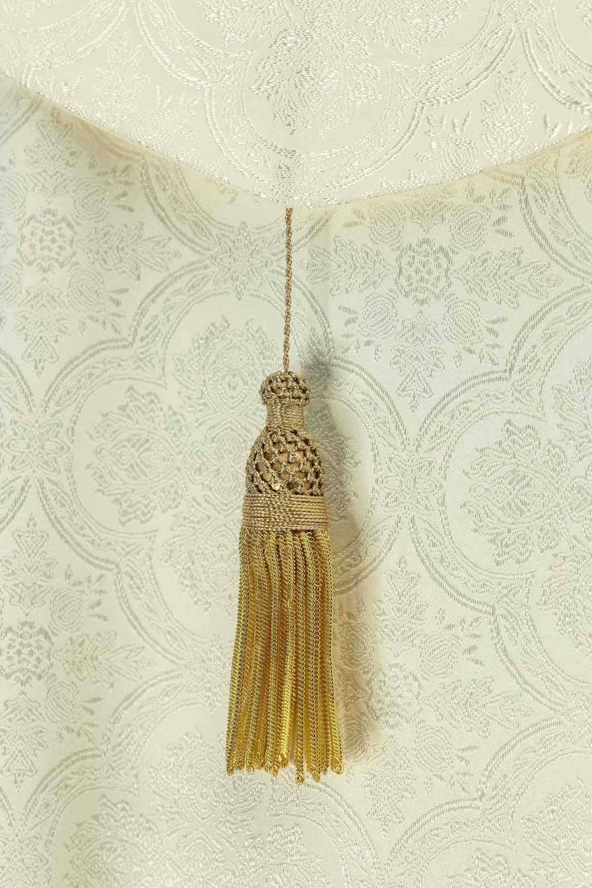 Ecru jacquard cope back detail showing the gold tassel and woven pattern