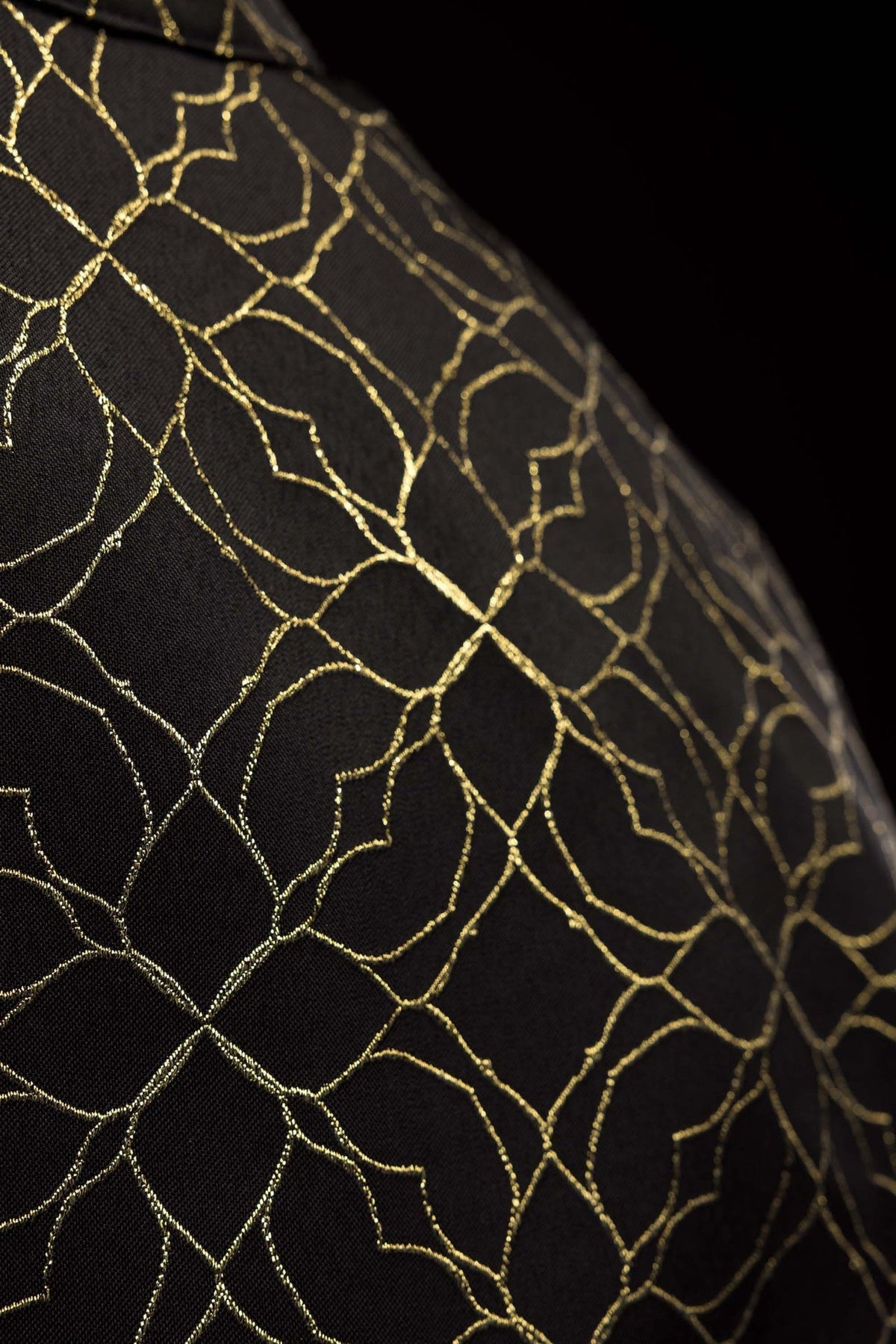 Black cope fabric close-up showing repeating gold floral jacquard pattern