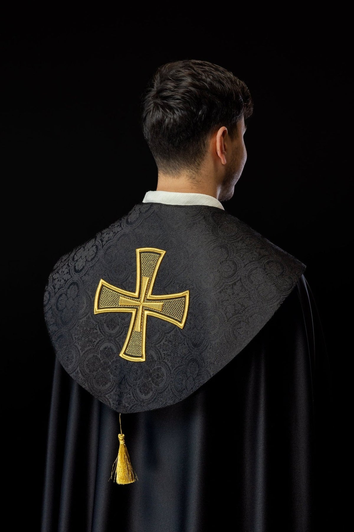 Black cope back view with gold cross embroidery and tassel