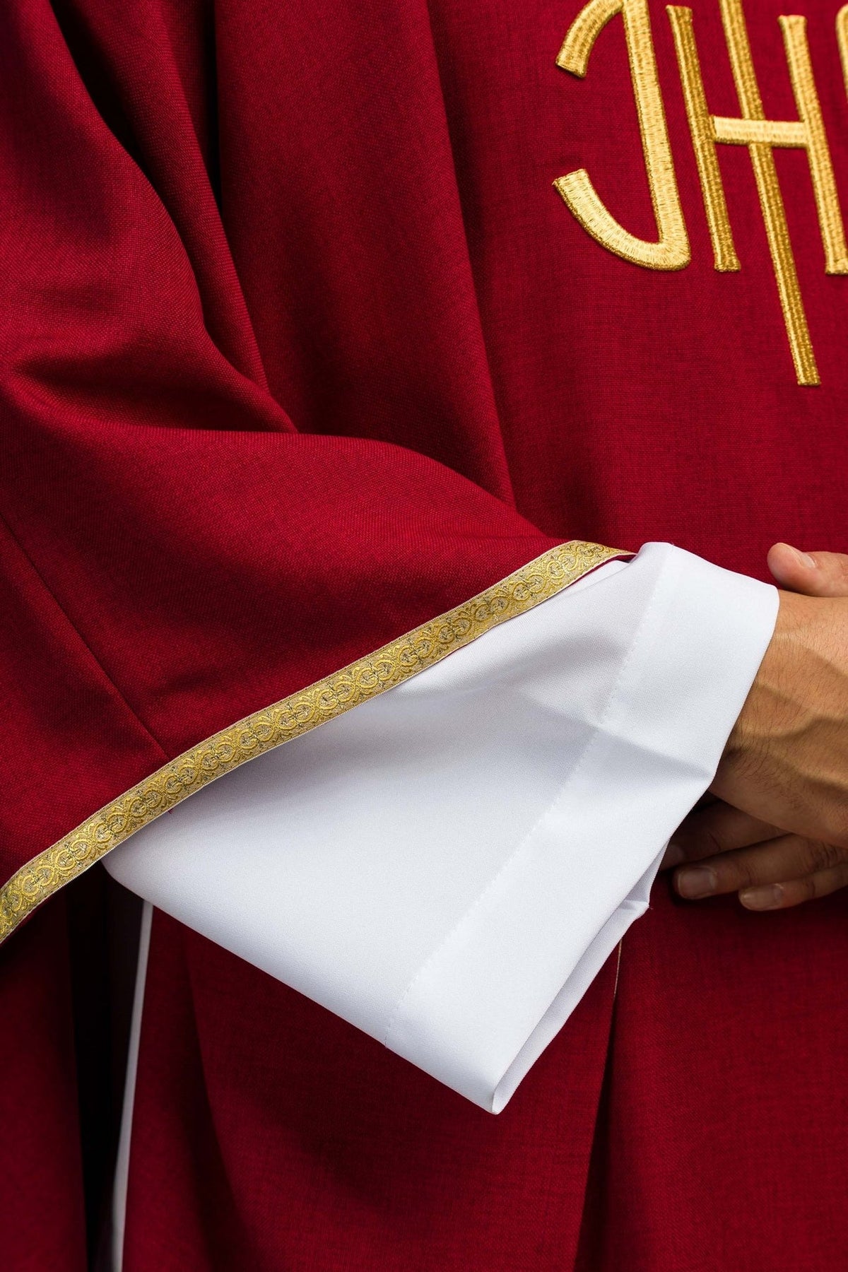 Red chasuble close-up showing gold IHS embroidery and sleeve trim