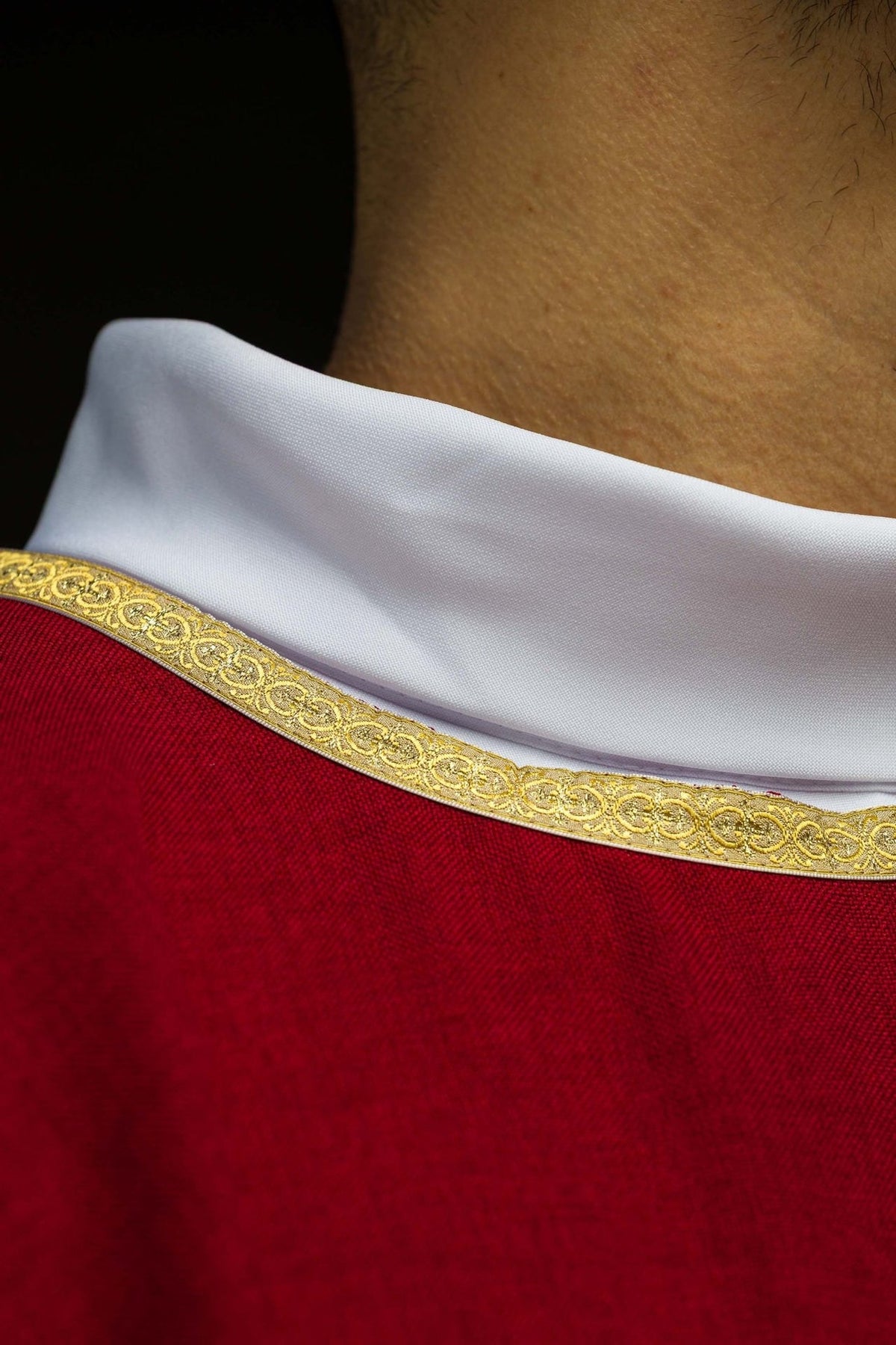 Red chasuble close-up showing gold trim and white sleeve
