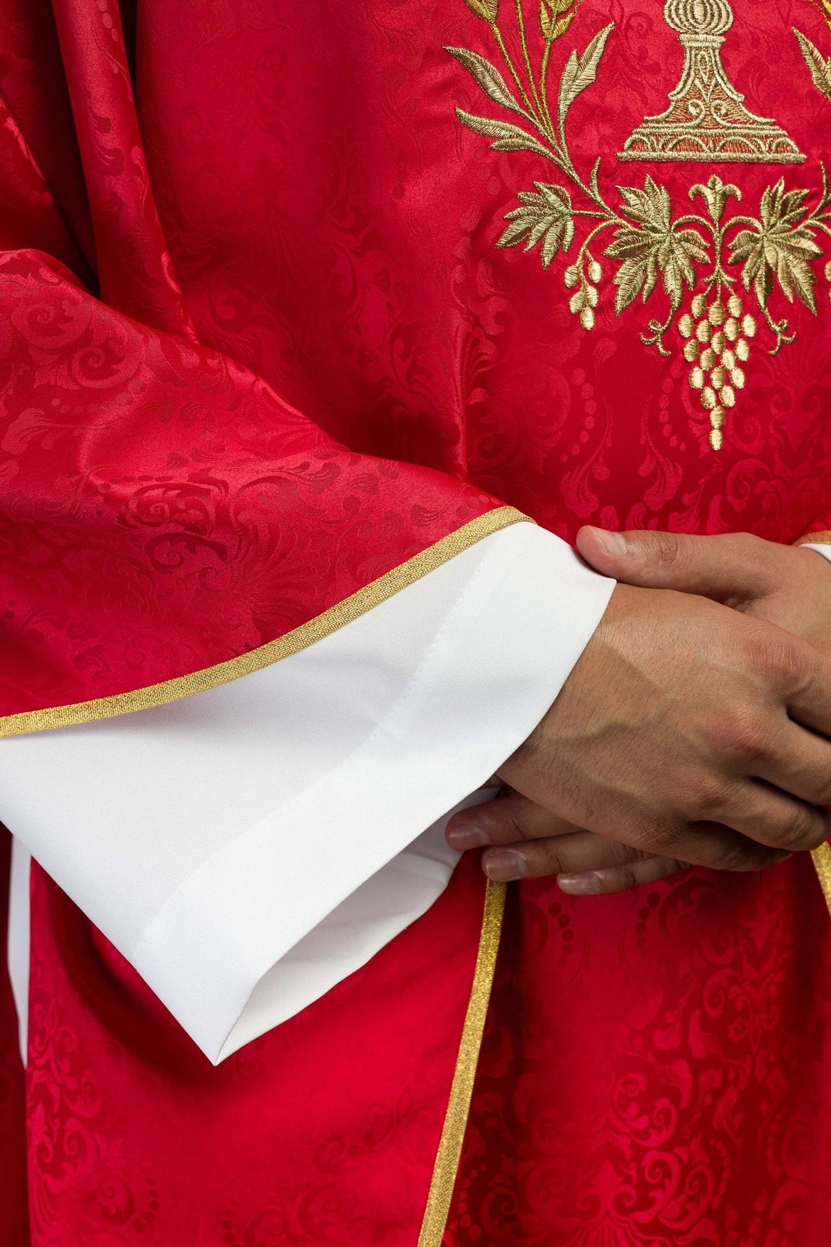 Red chasuble detail showing gold trim and white sleeve cuffs