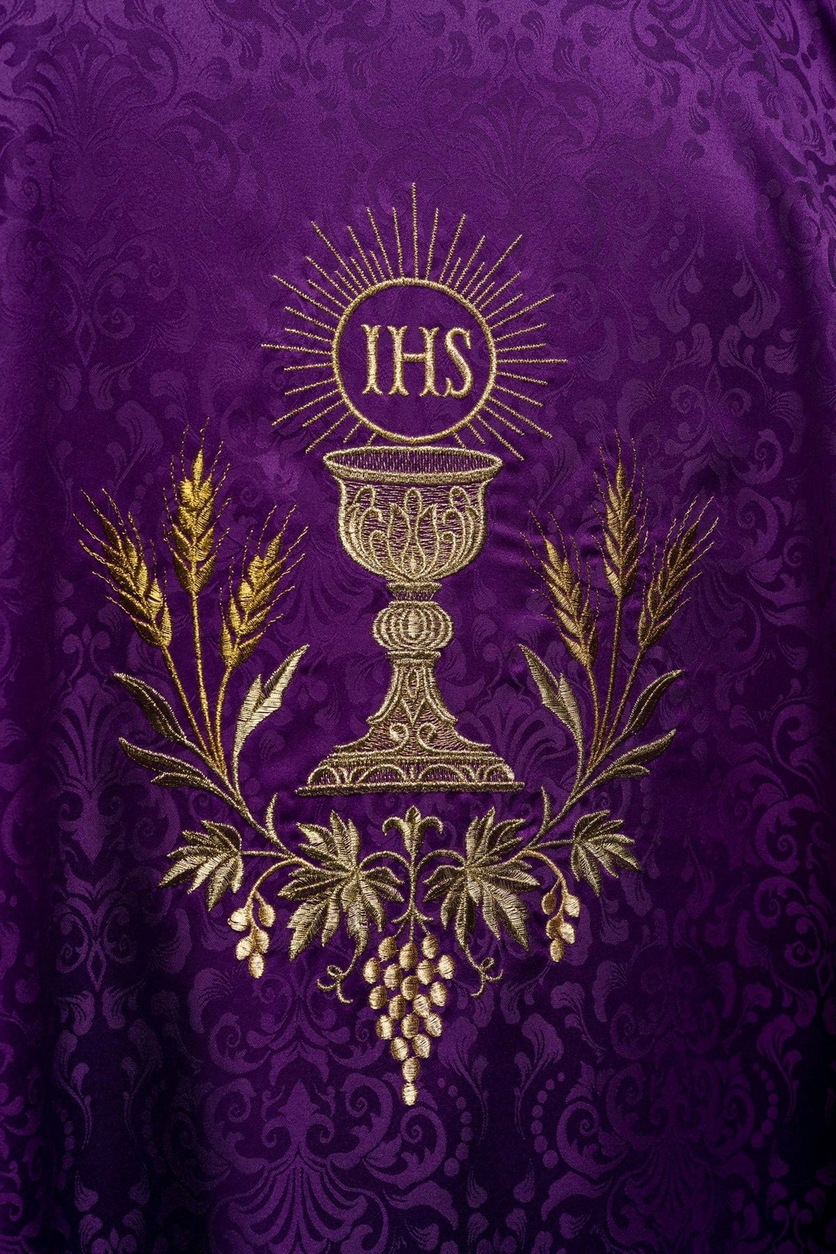 Purple chasuble embroidery close-up showing gold chalice, IHS monogram, wheat and vine