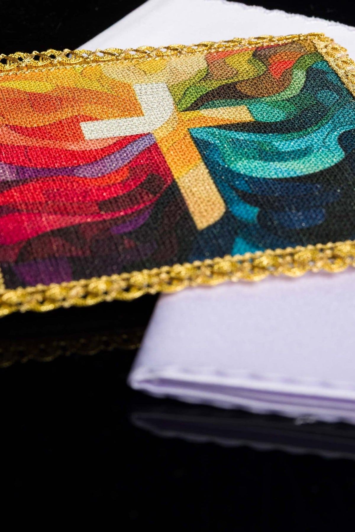 Altar linen set detail showing colorful cross panel and folded white linen
