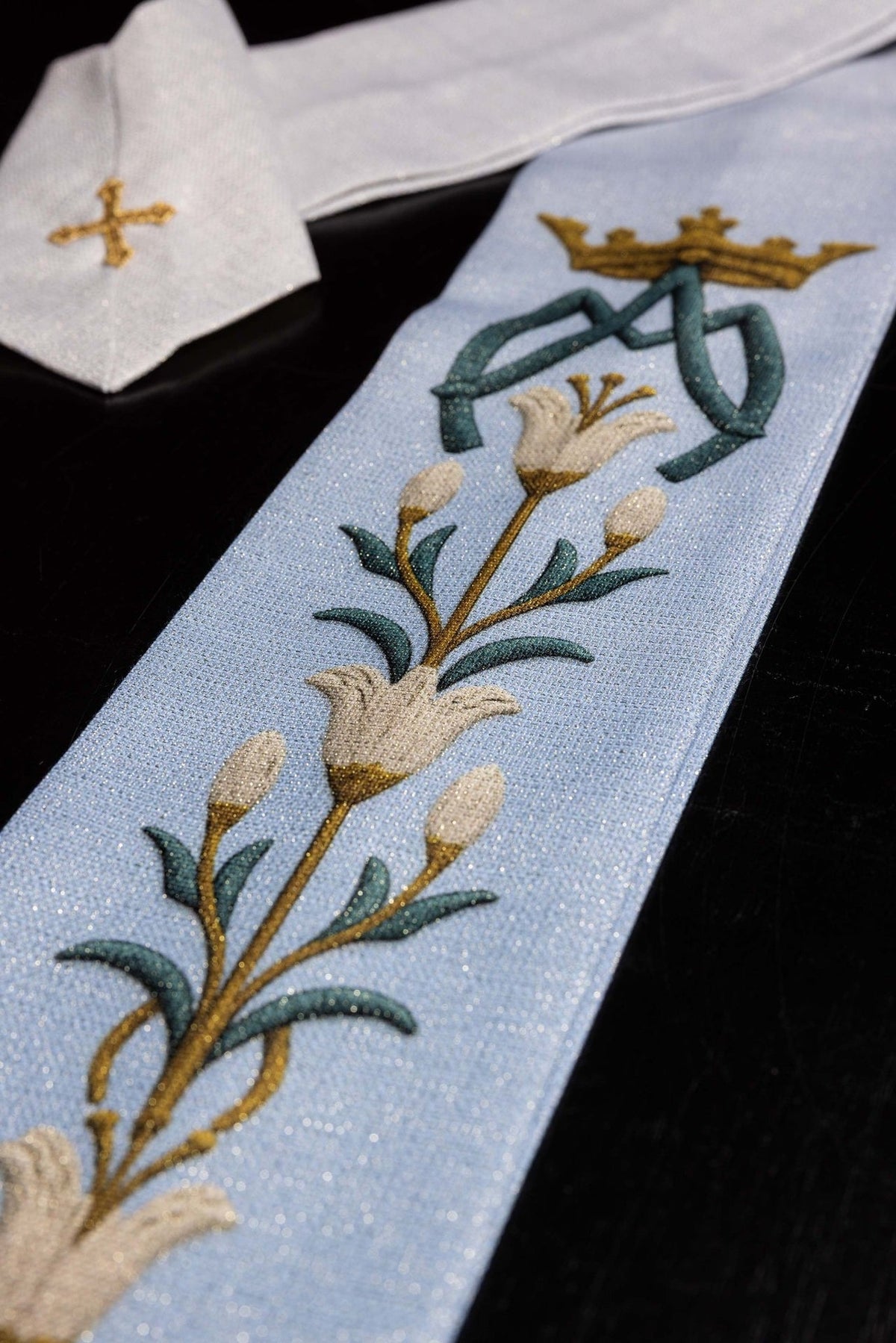 Light blue Marian chasuble close-up with ecru lily embroidery and gold AM monogram