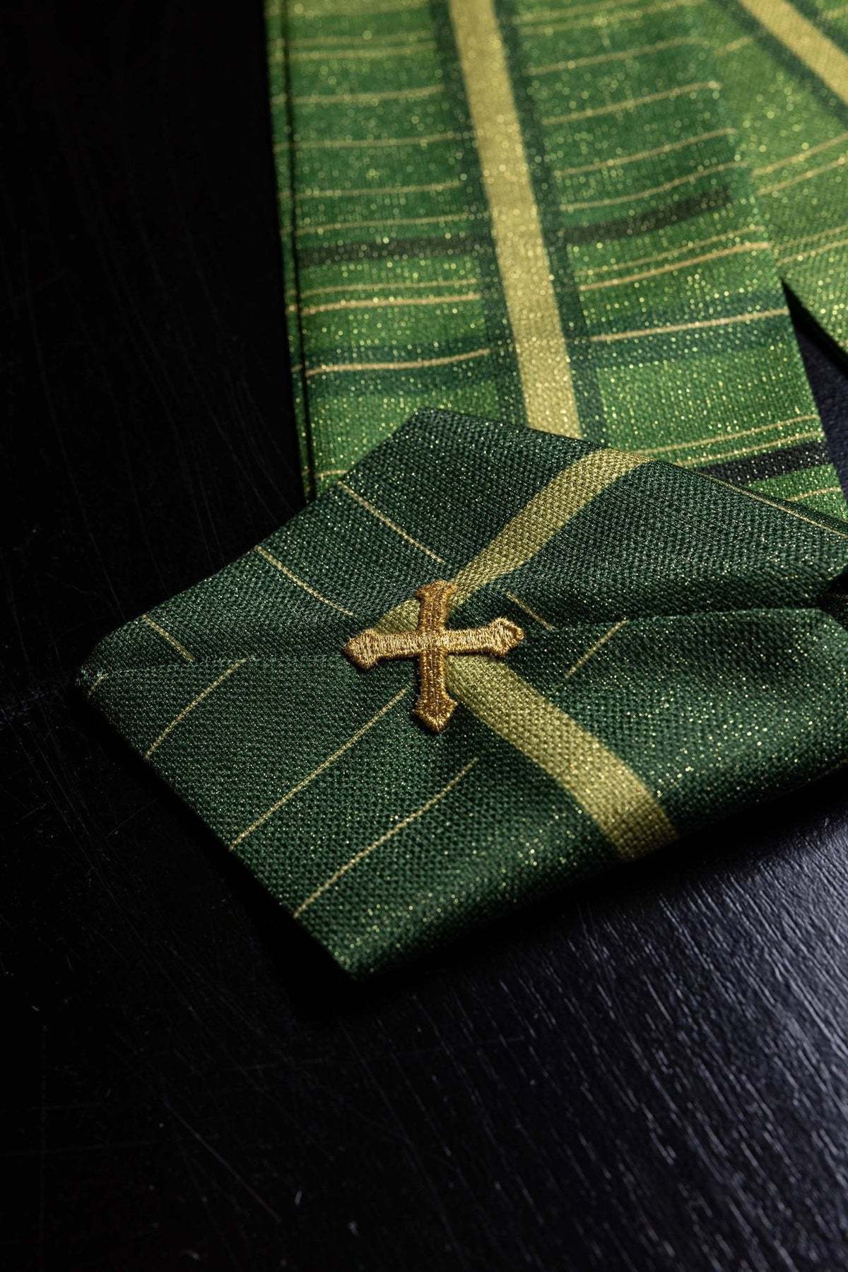 Green chasuble close-up showing gold embroidered cross and cross-patterned fabric