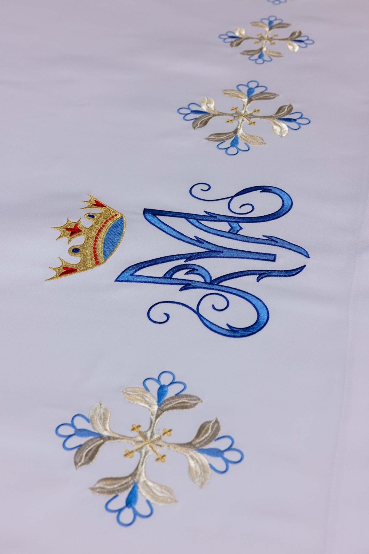 Altar cloth close-up showing blue Marian monogram, crown and embroidered floral motifs