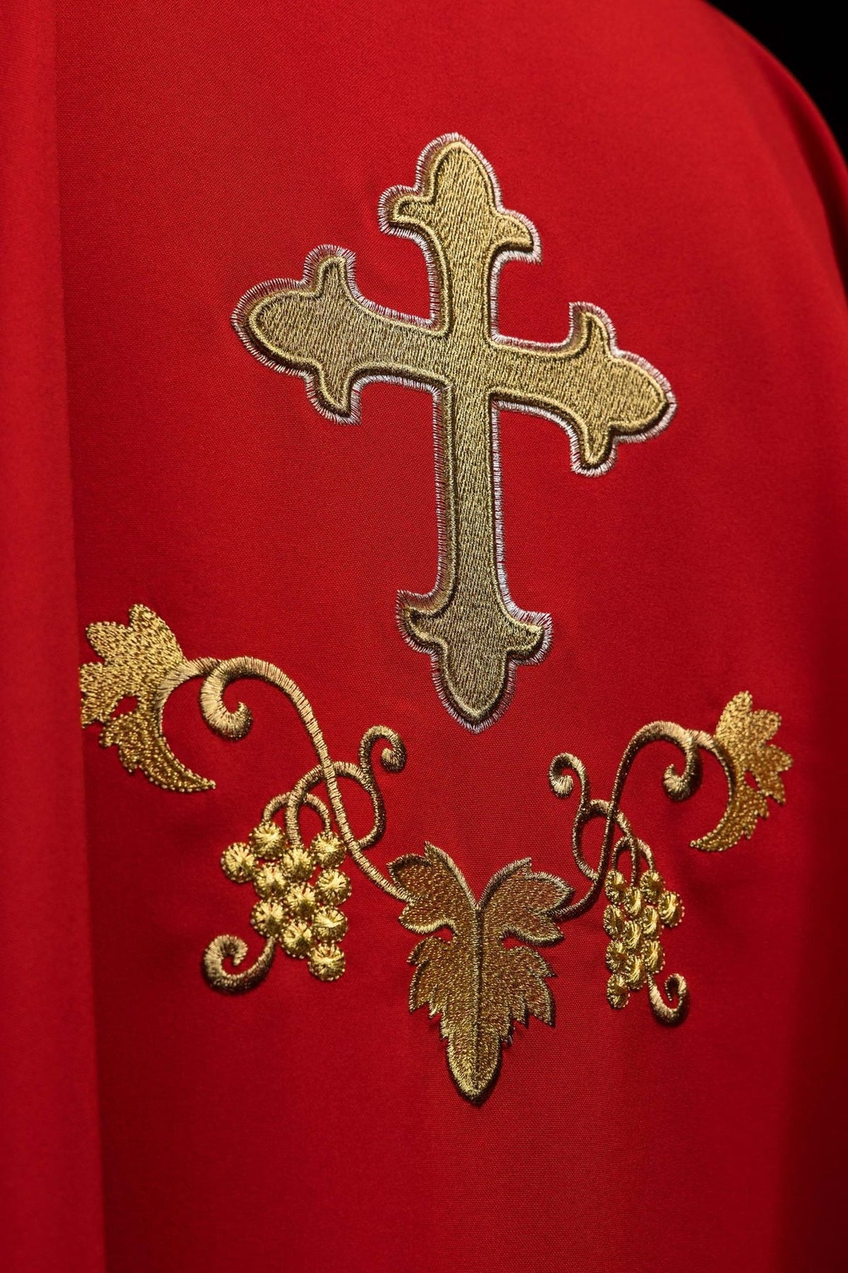 Red chasuble close-up showing embroidered gold cross and grape motifs