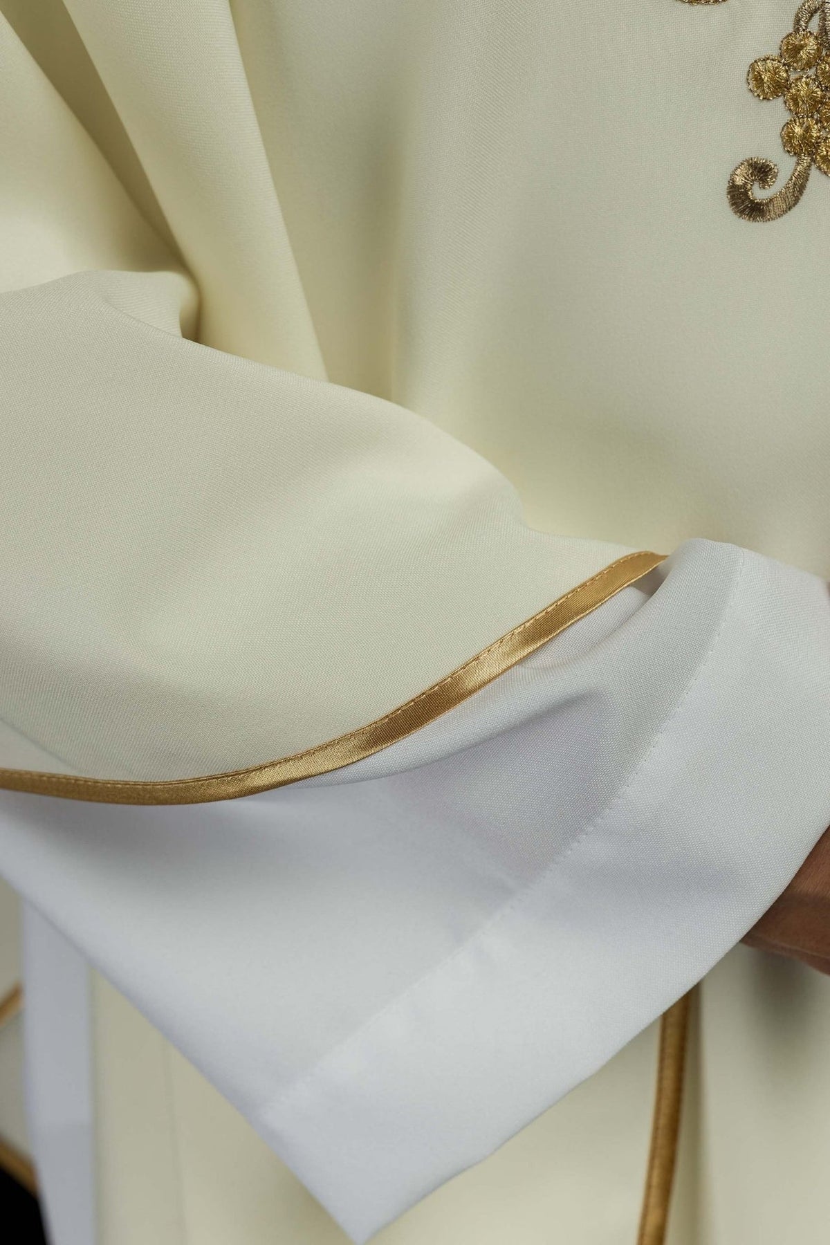 Embroidered chasuble sleeve close-up with gold trim and white cuff