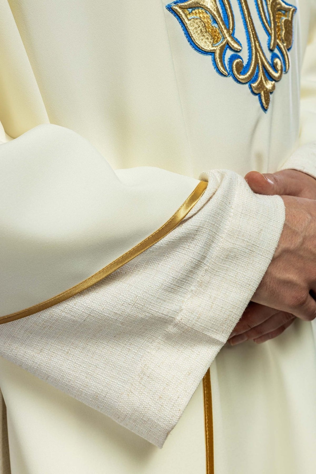 Chasuble detail showing ecru fabric and gold trim at the sleeve