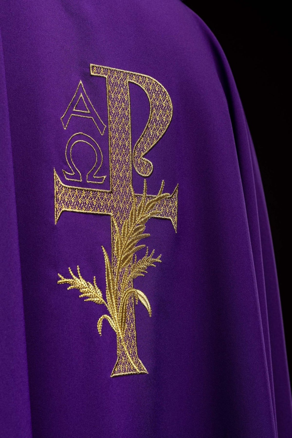 Purple chasuble close-up showing gold Alpha Omega cross embroidery