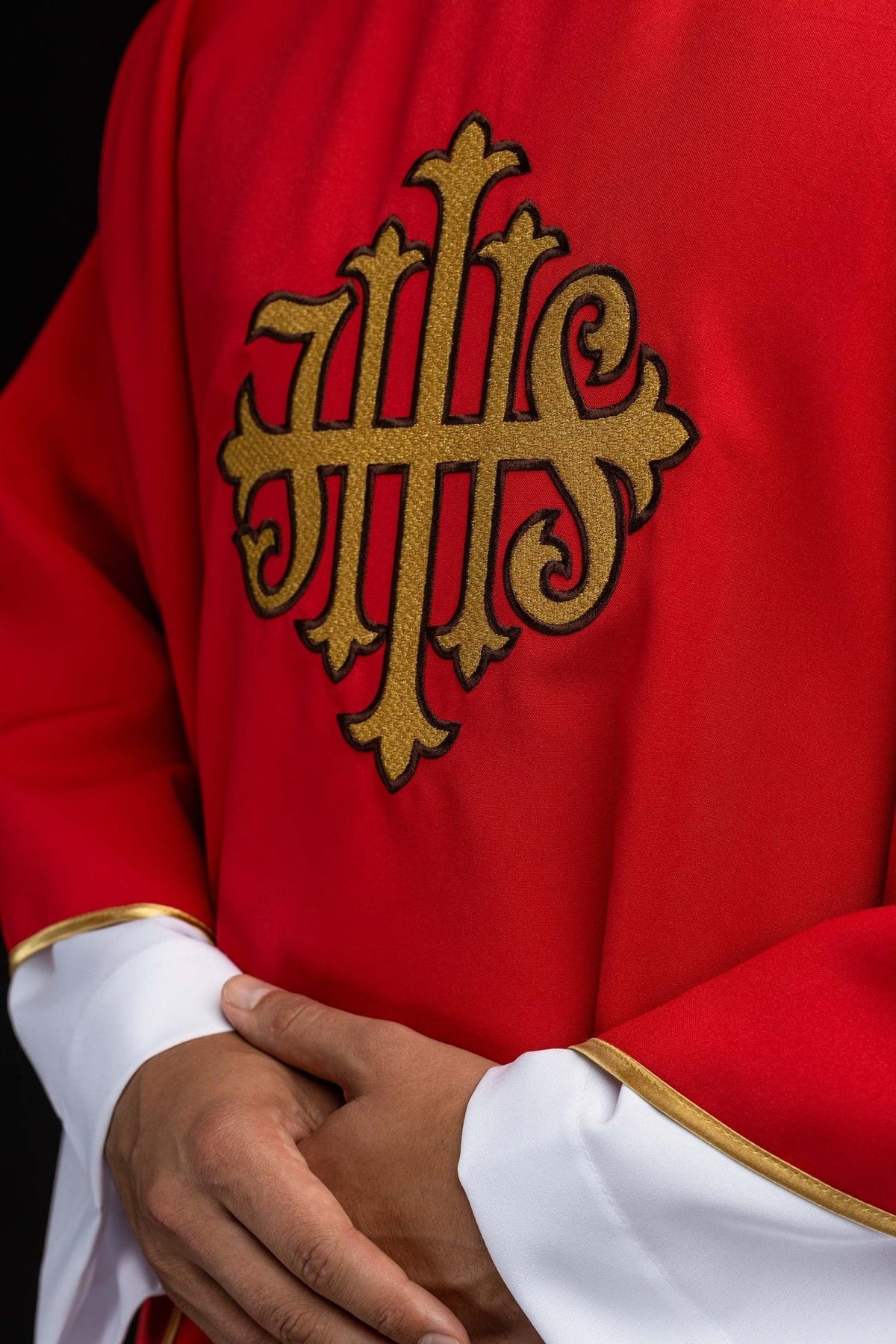 Red chasuble close-up showing gold embroidered JHS symbol and sleeve trim