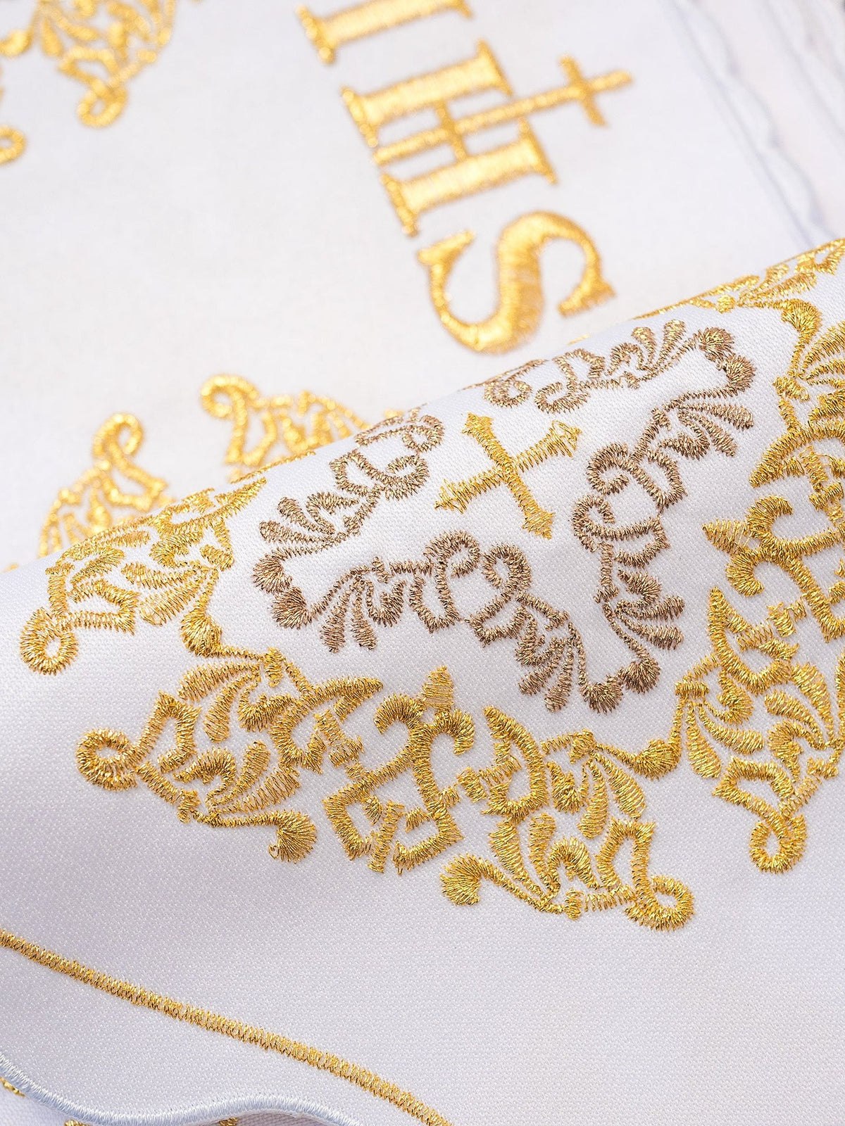 White altar lace close-up showing gold IHS, cross and rosette embroidery