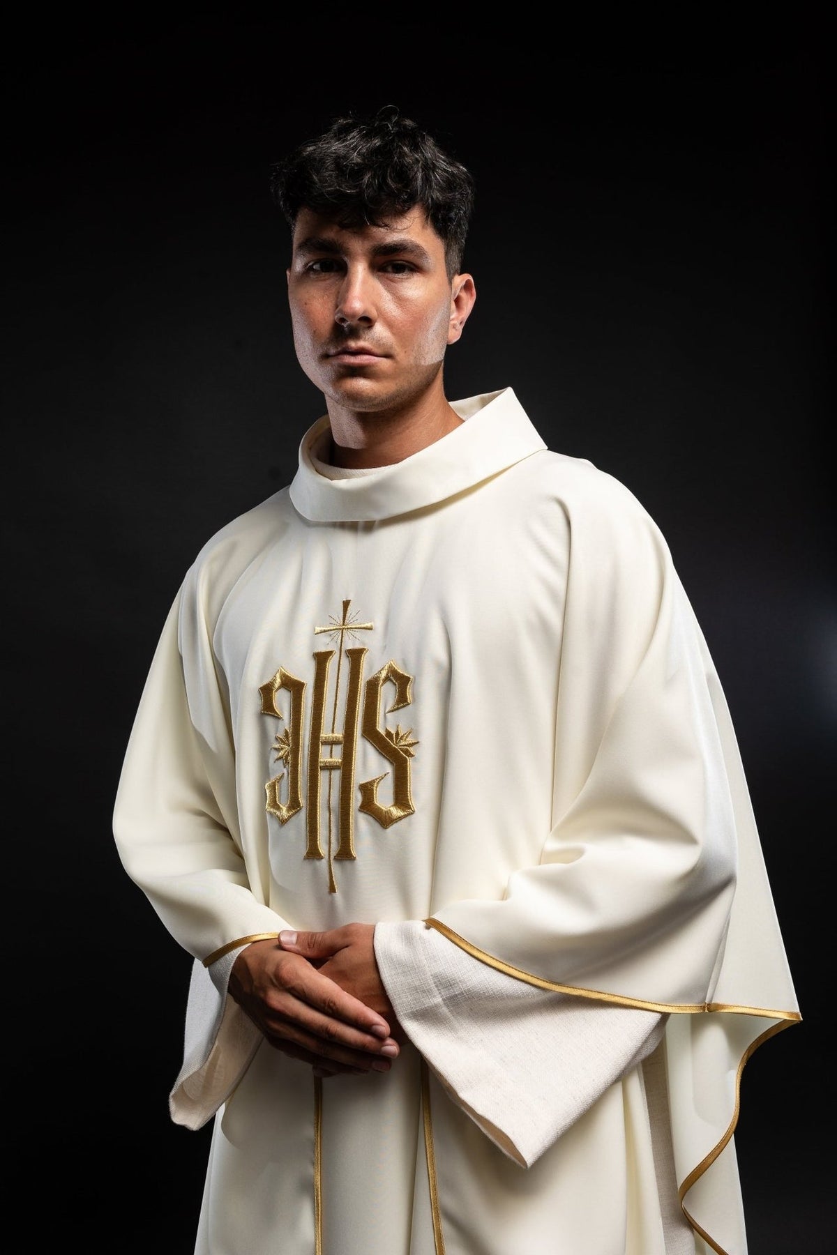 Ecru chasuble worn from the front, showing gold IHS embroidery and trim