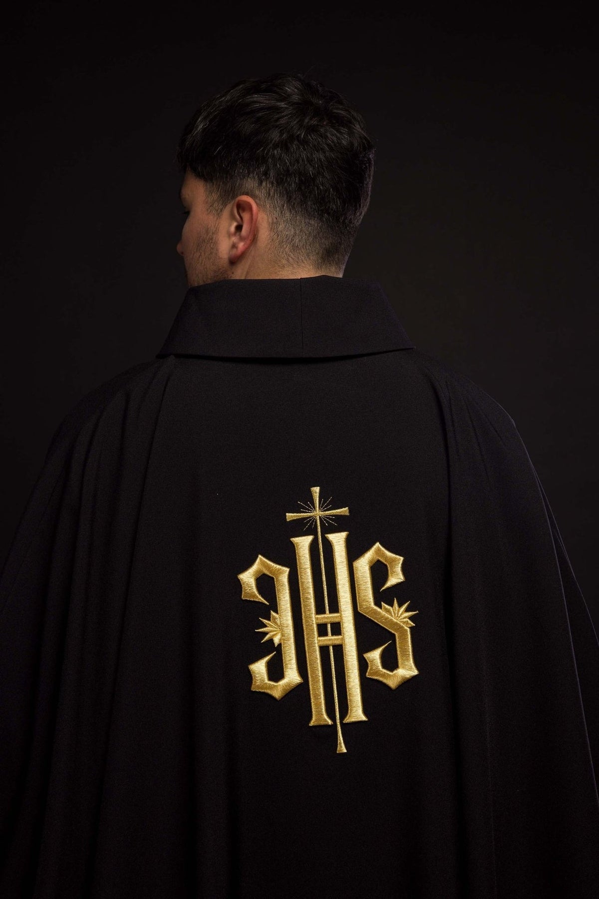 Black chasuble back view with large gold embroidered IHS symbol