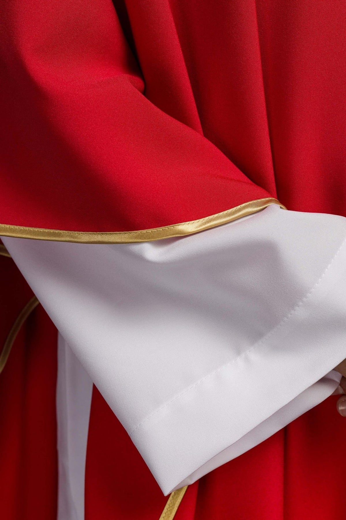Red chasuble close-up showing gold trim and white sleeve fabric