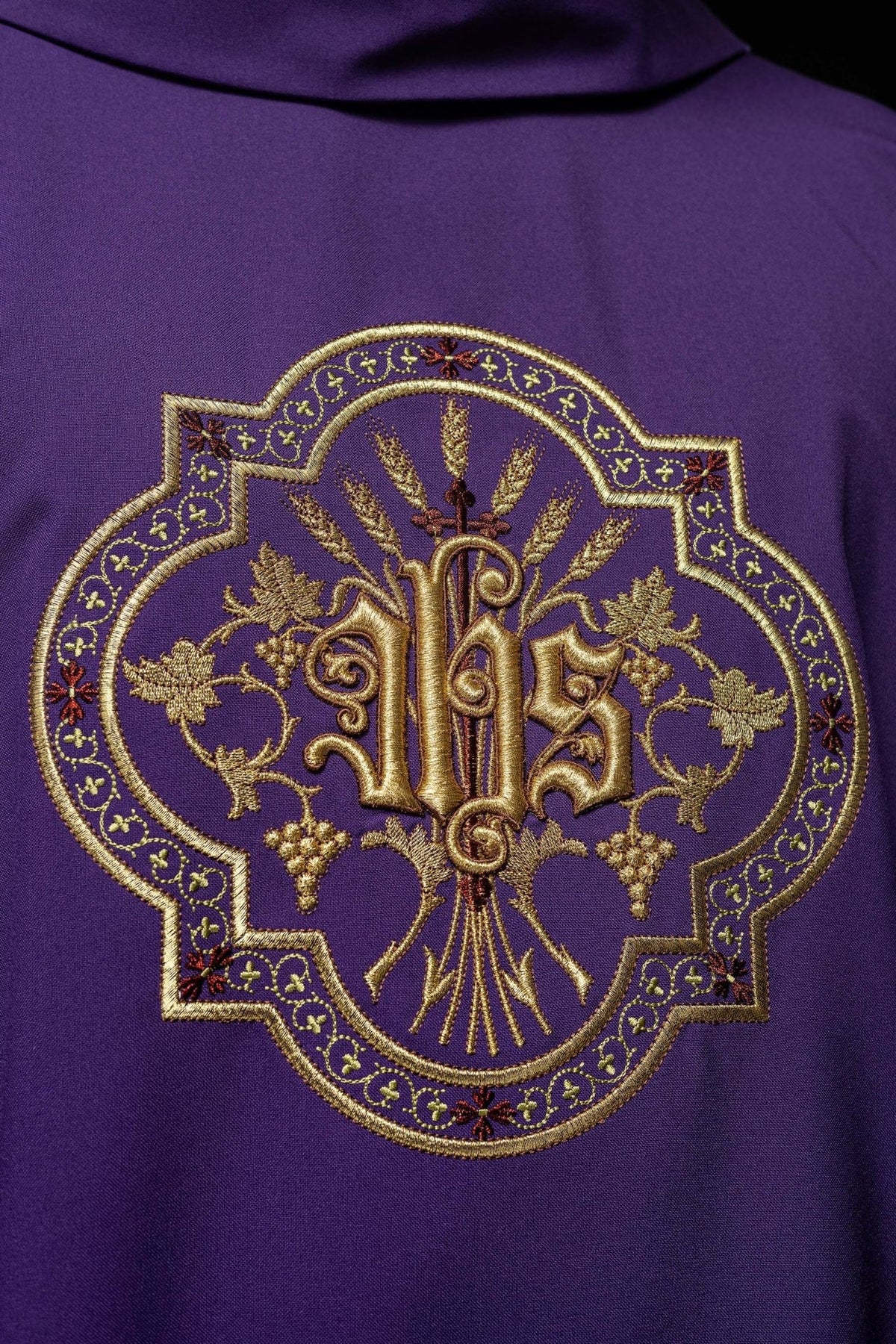 Purple chasuble close-up showing the gold IHS embroidery with grapes and wheat