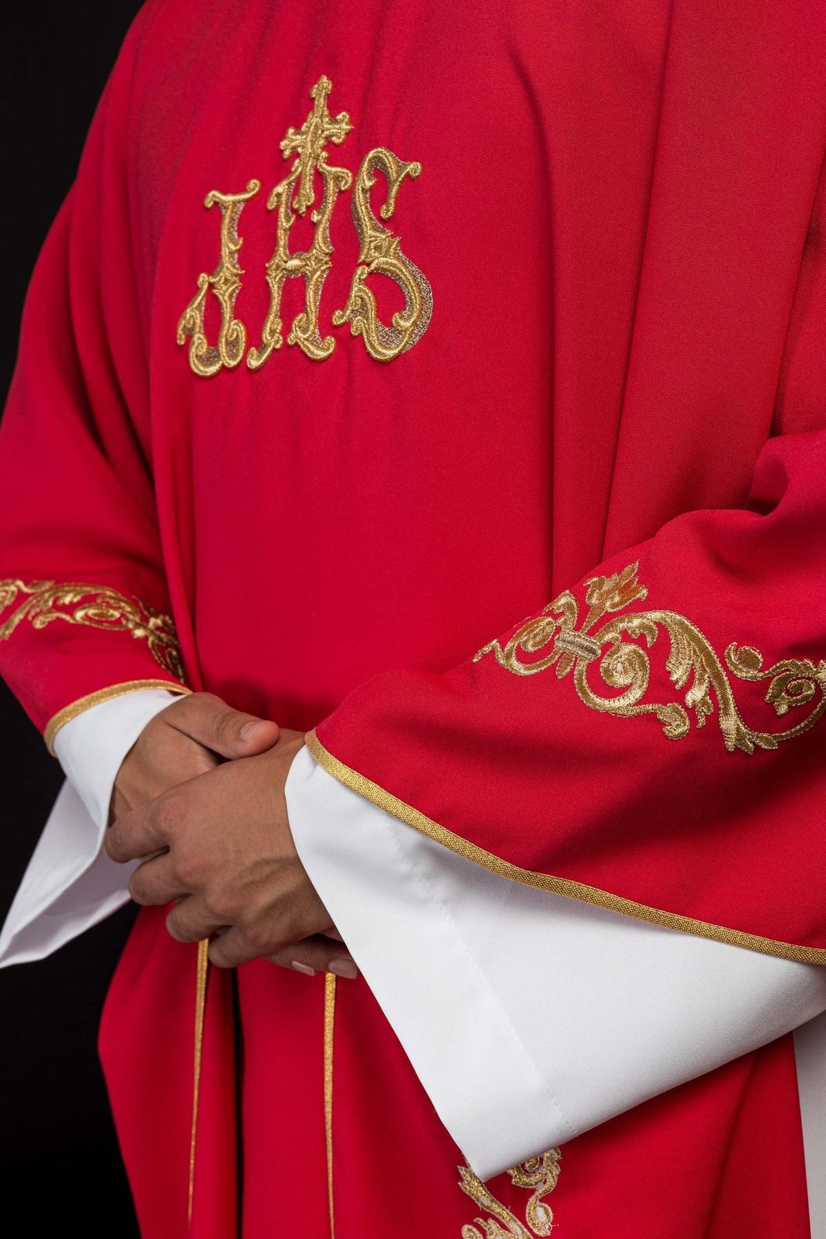 Red chasuble close-up showing gold IHS embroidery on the front