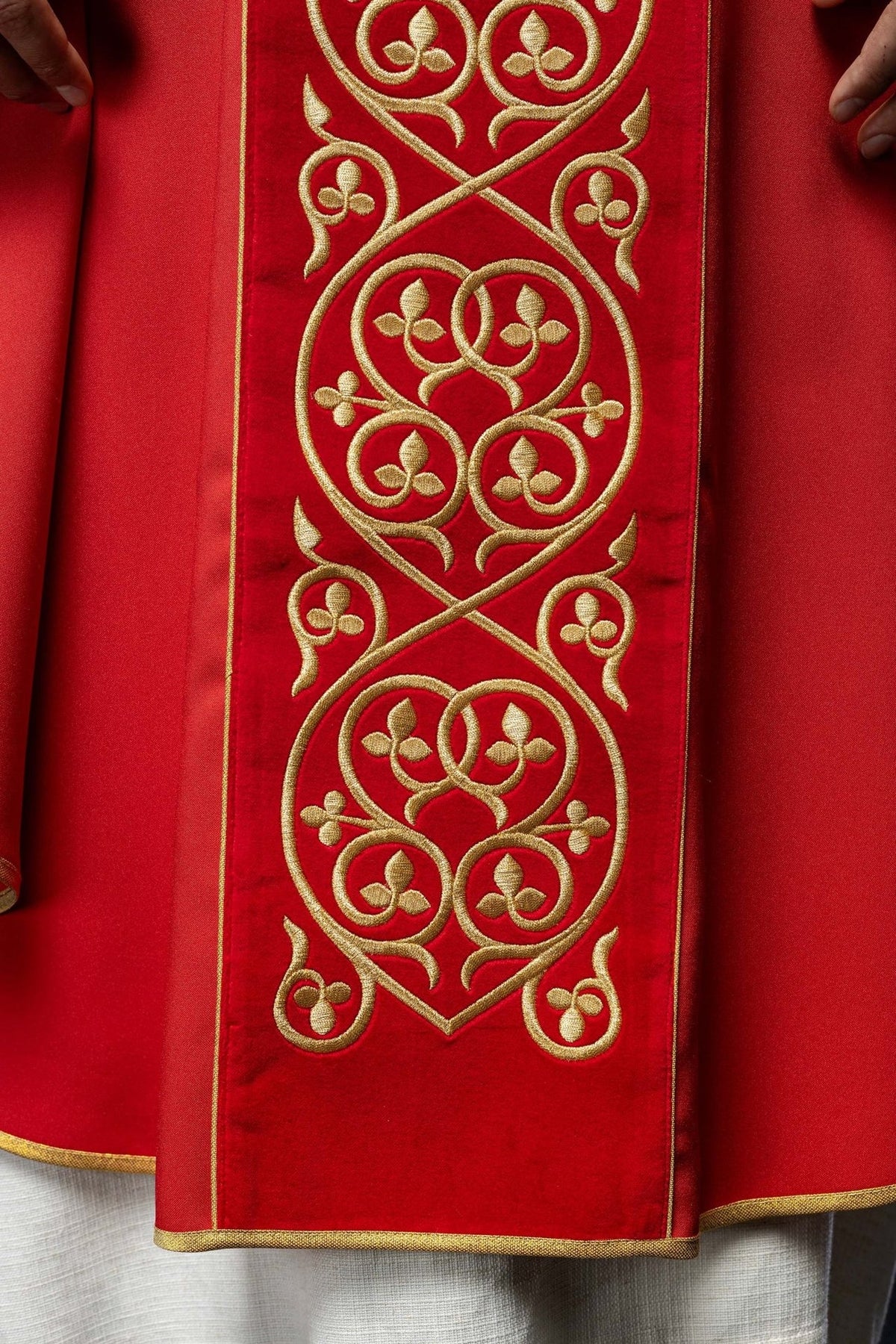 Red chasuble sleeve close-up with gold trim and embroidered orphrey