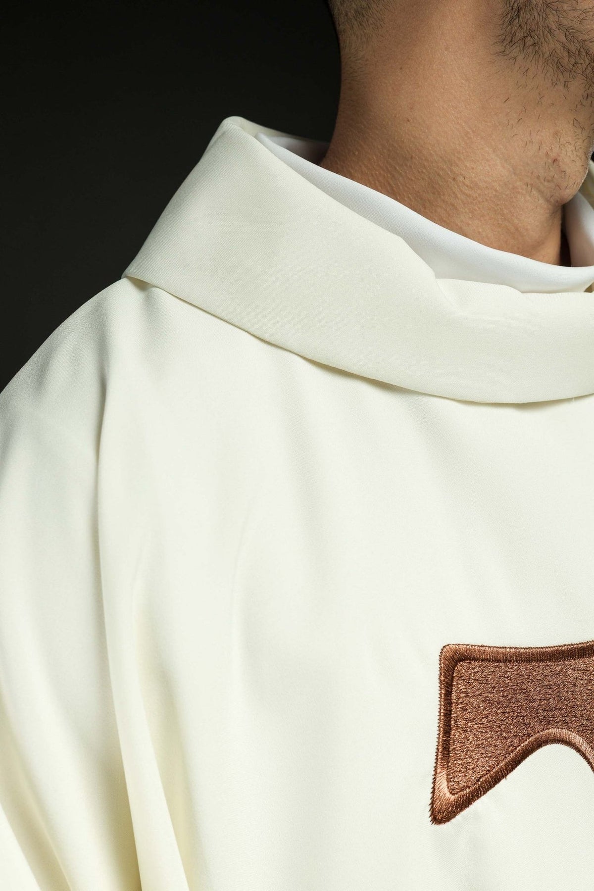 White chasuble close-up with a stand-up collar and part of the brown TAU cross