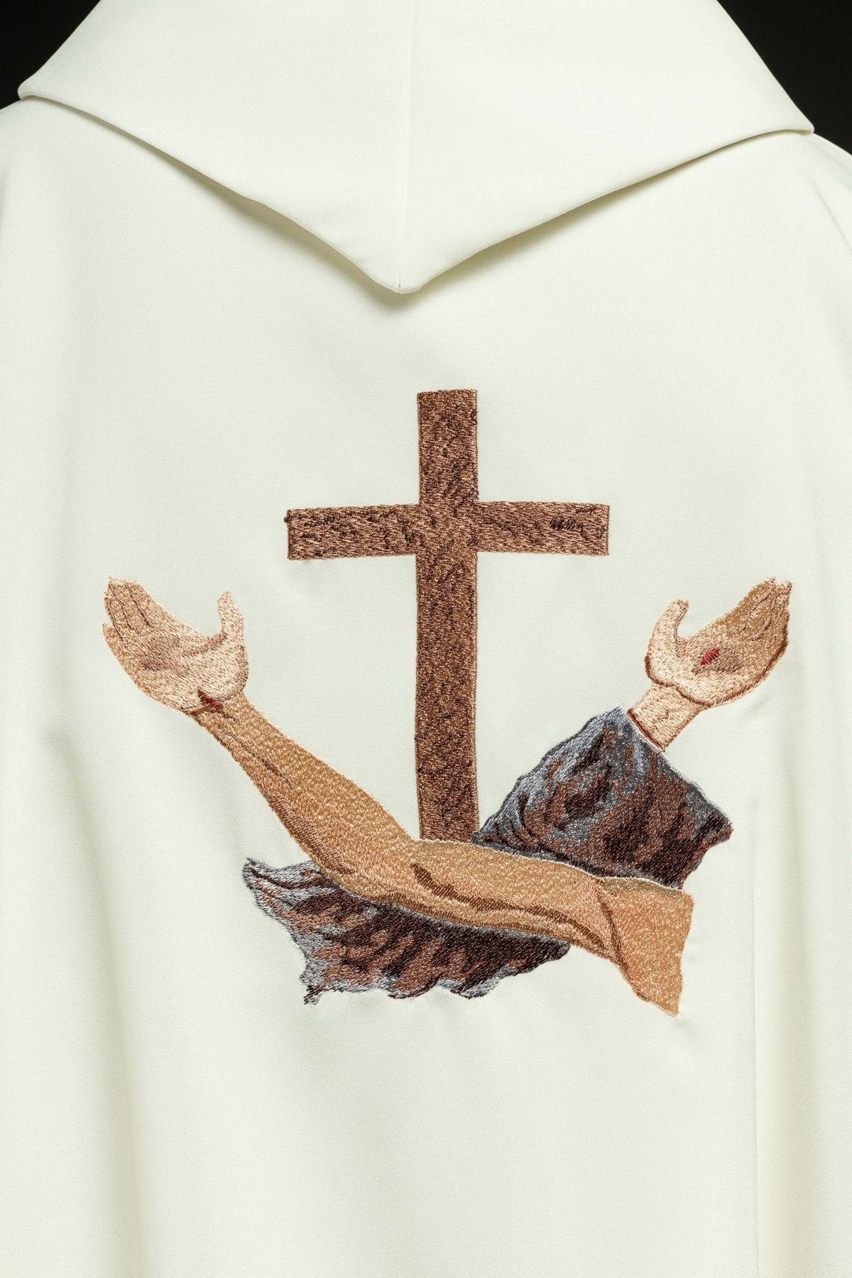 Back embroidery detail on the white chasuble showing a brown cross and crossed arms