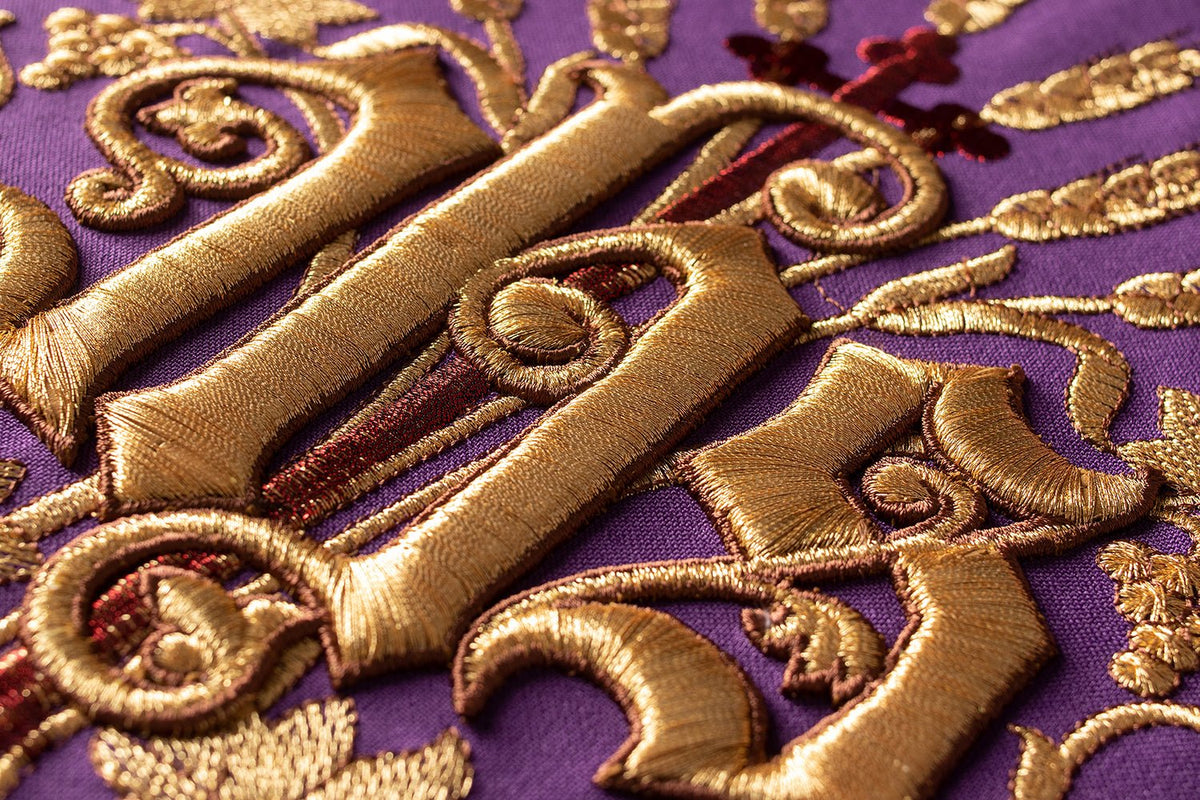Close-up of embroidered gold IHS motif on purple Roman chasuble