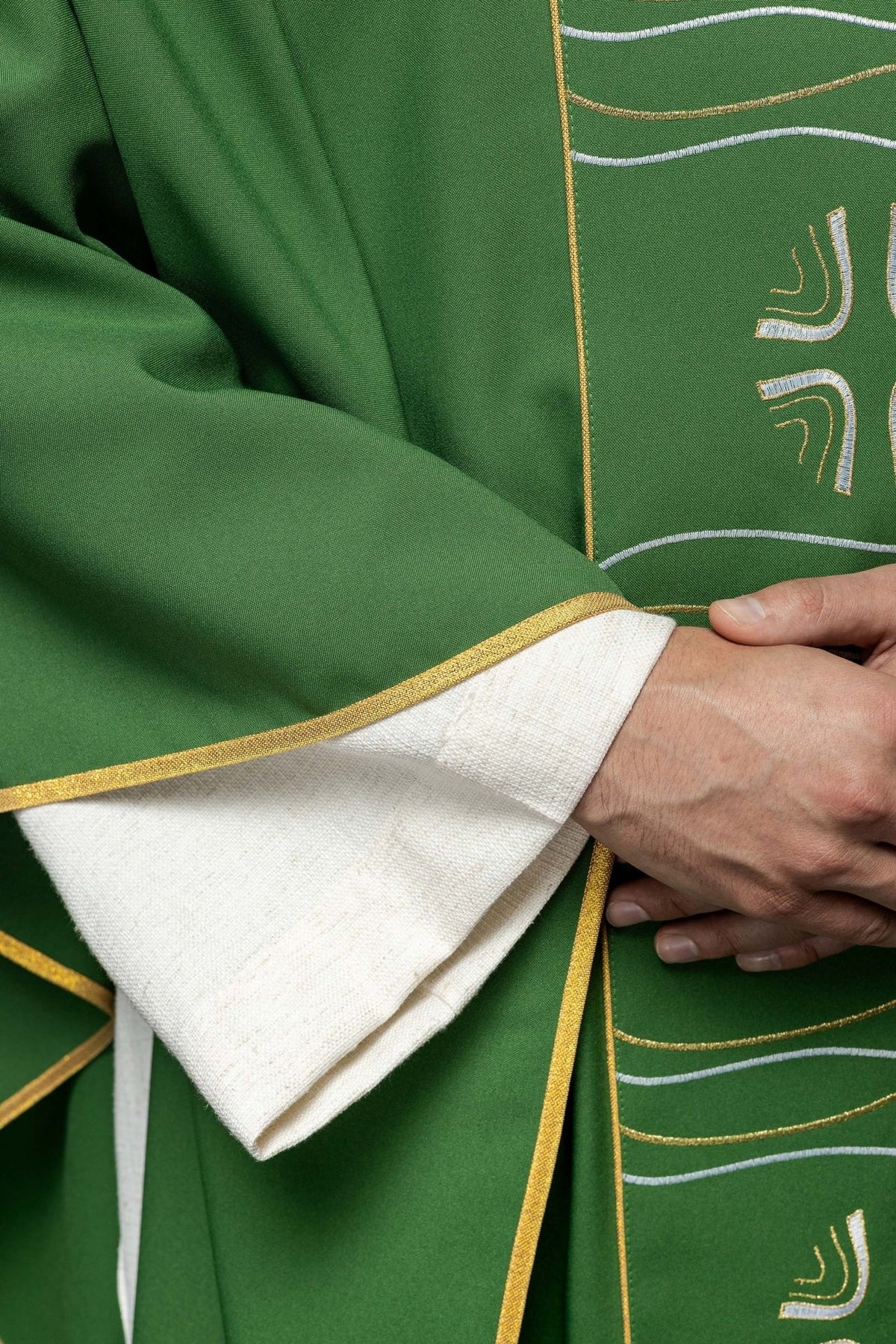 Green chasuble close-up showing gold trim at the sleeve edge and embroidered cross