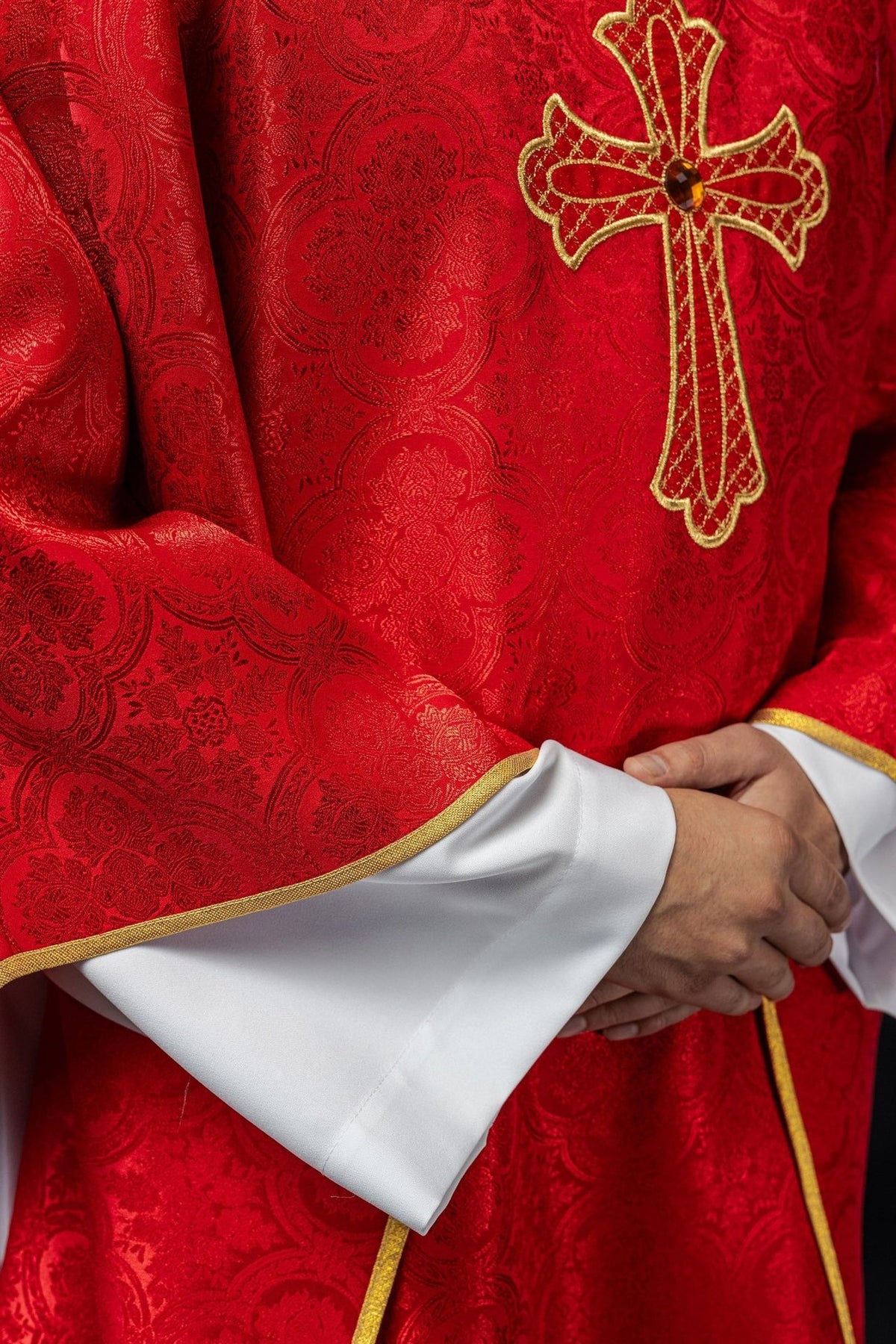 Red chasuble side close-up showing gold trim, patterned fabric and cross embroidery